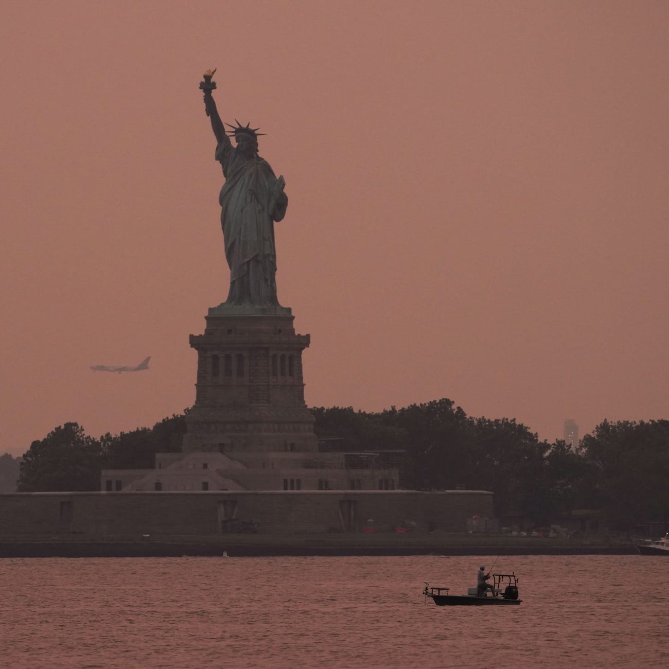 The Statue of Liberty is seen at sunset through haze caused by smoke from Canadian wildfires, as viewed from Brooklyn, New York, August 5, 2025.