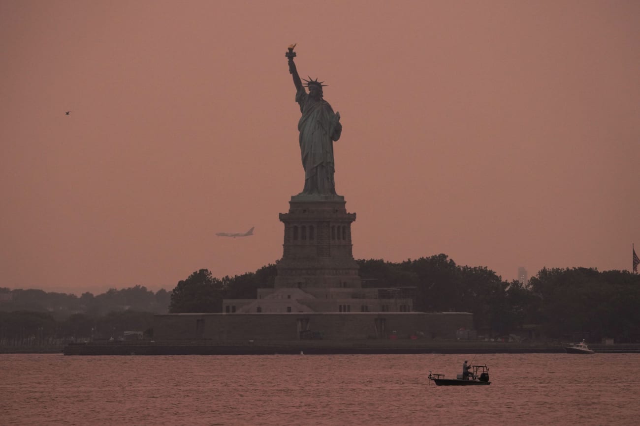 The Statue of Liberty is seen at sunset through haze caused by smoke from Canadian wildfires, as viewed from Brooklyn, New York, August 5, 2025.