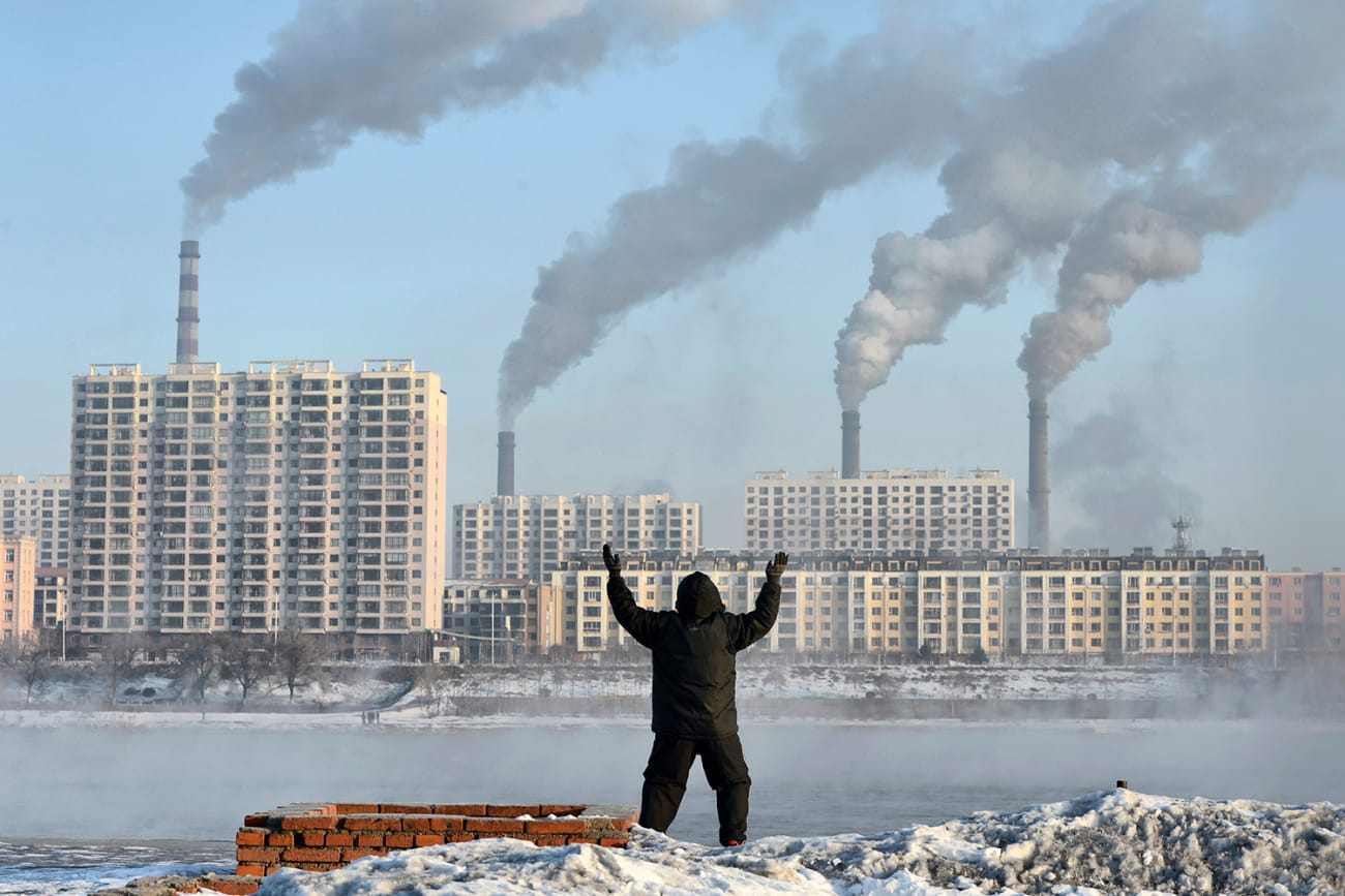 Factories emit smoke in Jilin province, China, across the Songhua River from where an elderly man exercises on the morning of Feb 24, 2013, after Chinese authorities announced plans to curb pollution. The photo shows the man in the foreground, back to the camera, with buildings on the other side of the river pouring out smoke. REUTERS/Stringer
