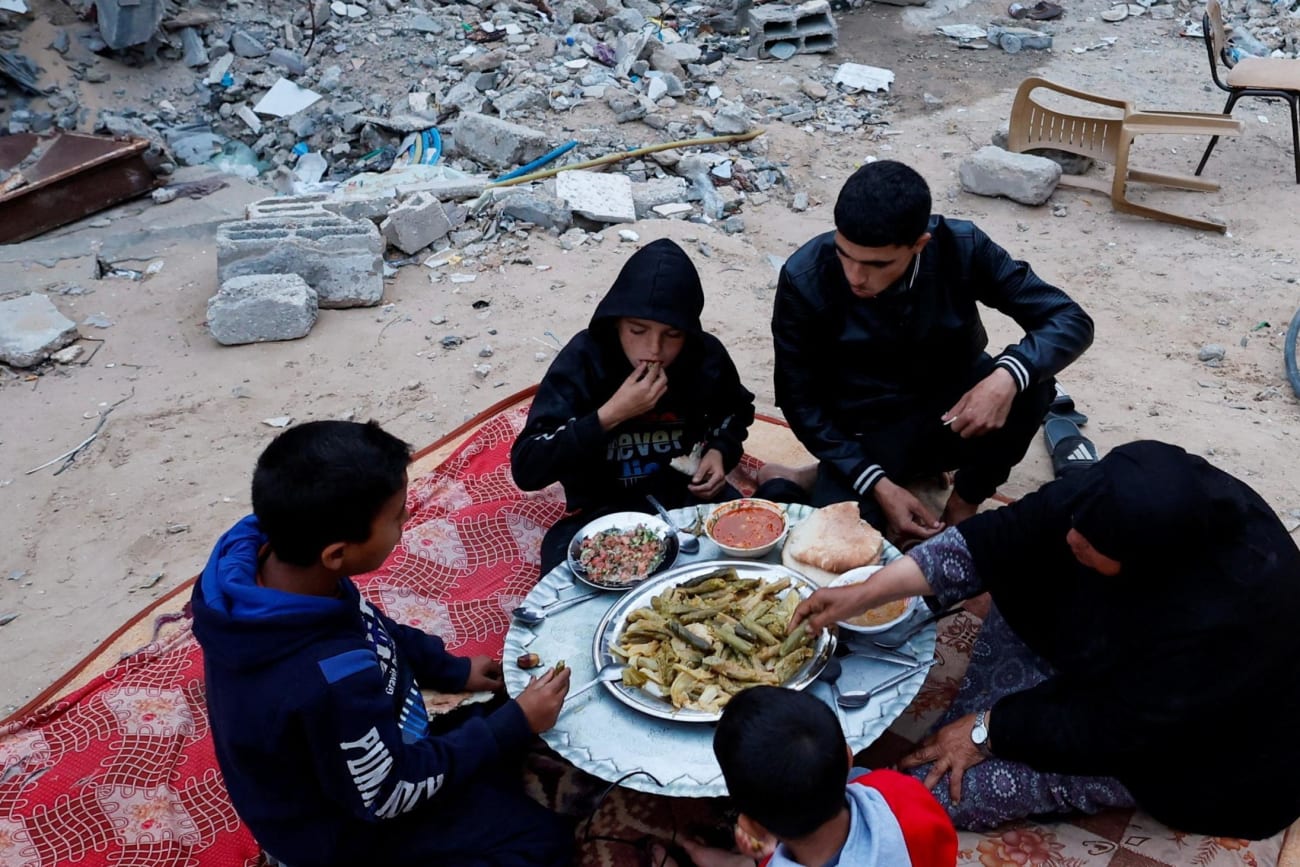 A Palestinian family eats their iftar meal they break their fast near the rubble of their destroyed house.