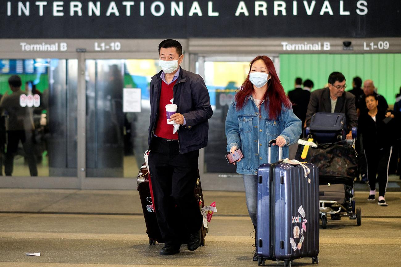 Image shows two travelers with their bags marching out of a gate that says 