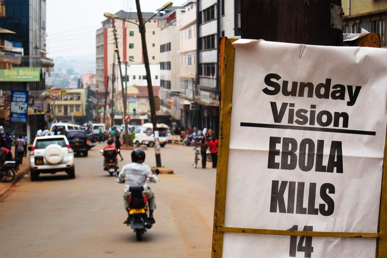 The photo shows a busy urban street with a sign announcing the Sunday paper's headline, Sunday Vision, EBOLA KILLS 14, Sunday July 29, 2012. 