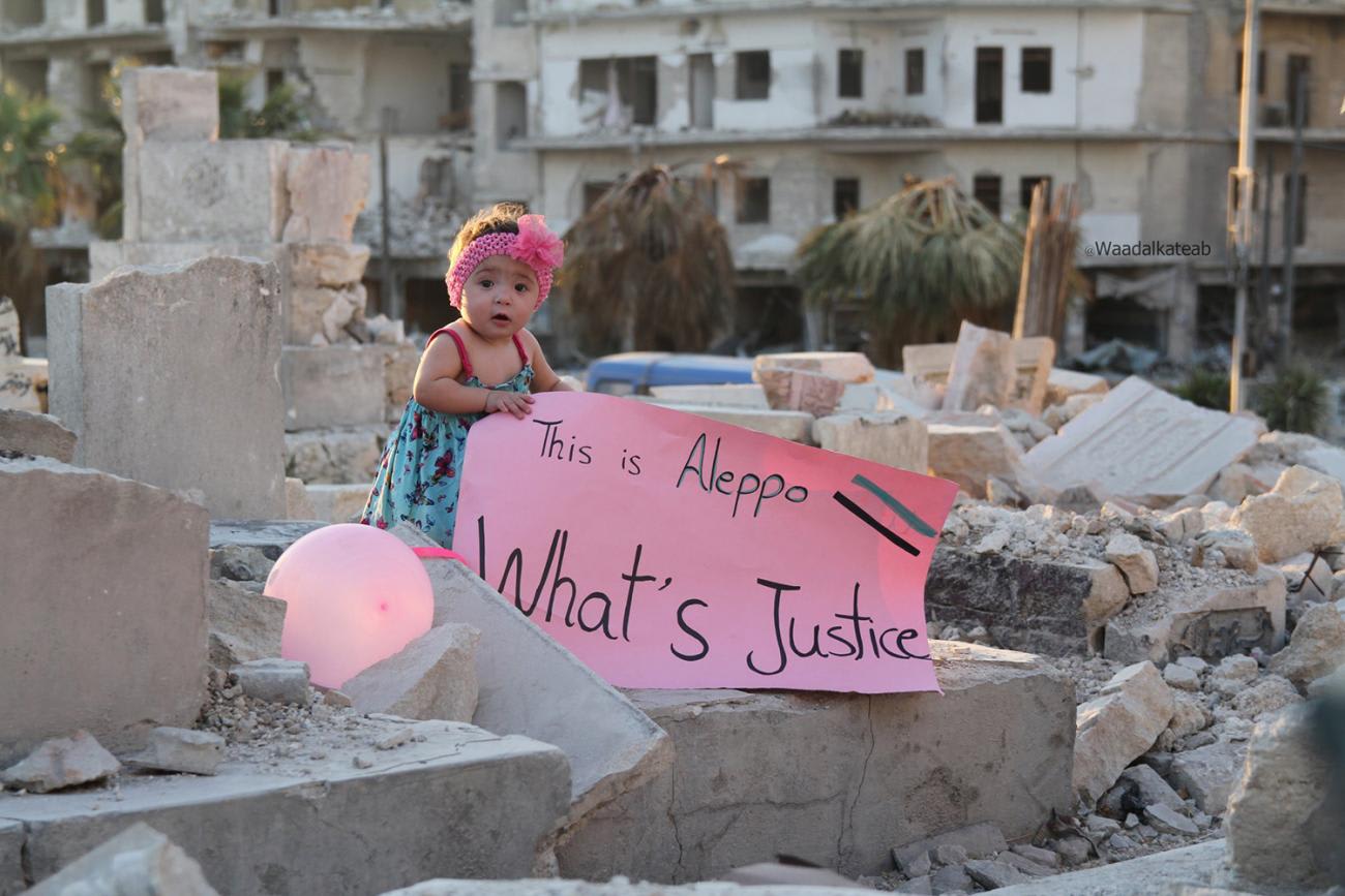 The picture shows the girl, a baby, really, standing on a pile of rubble amidst the destruction of the city holding a sign that reads,