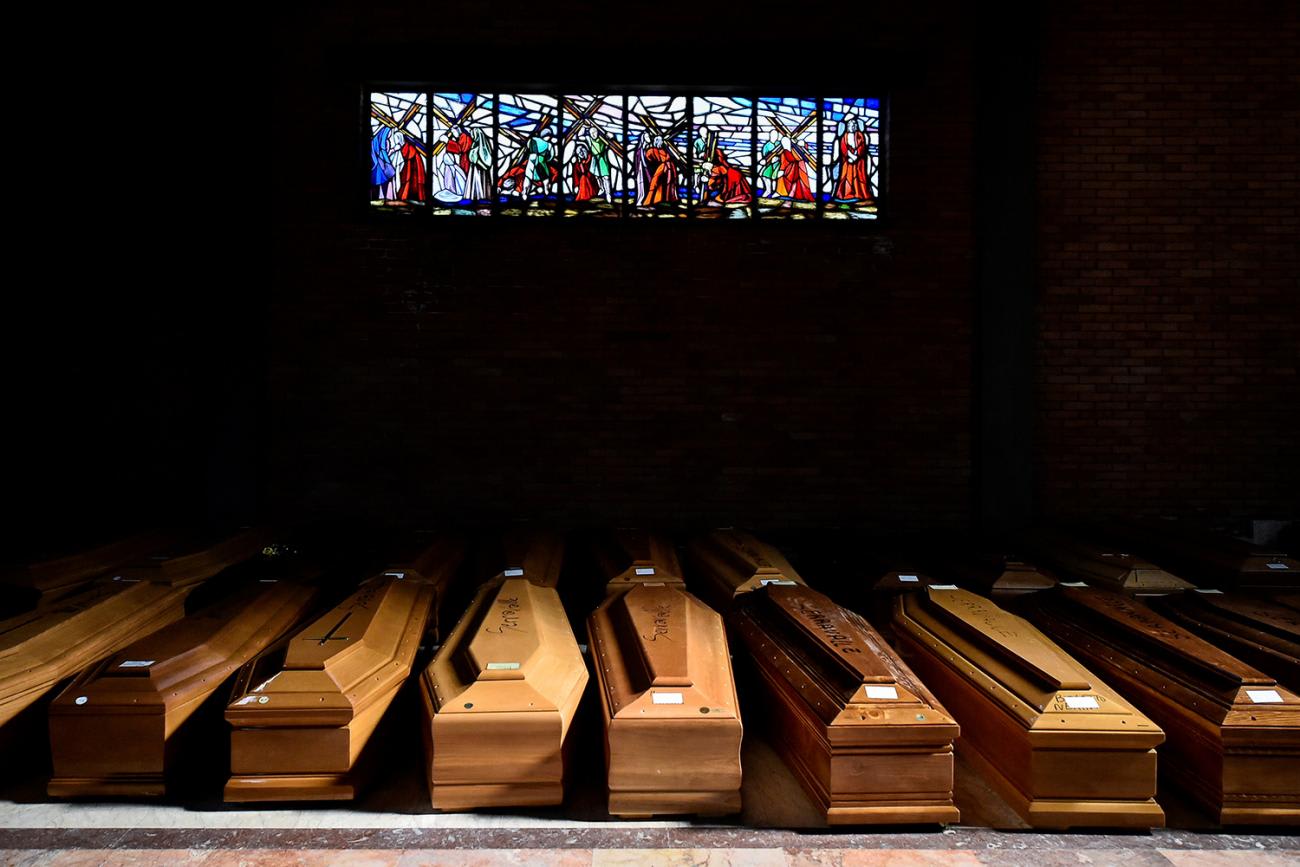 The image shows a huge number of plain coffins in a dimly lit corner of a church beneath a stained glass.