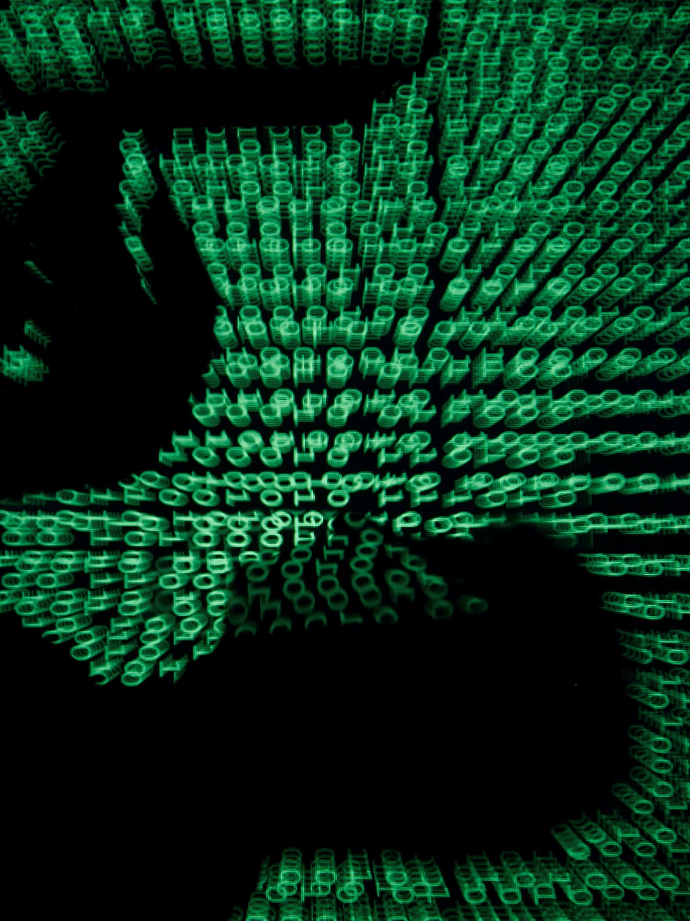 The image shows the silhouette of a man on a laptop with green ones and zeroes, reminiscent of the film "The Matrix" projected over the image. 