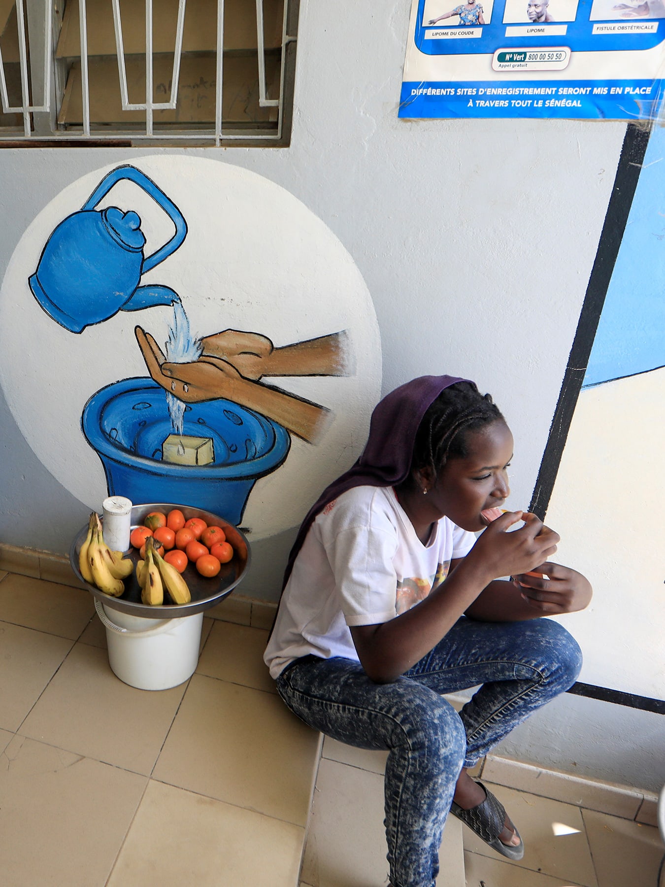 Picture shows a girl with a small basket of fruit sitting next to a large, blue UNICEF basin. 