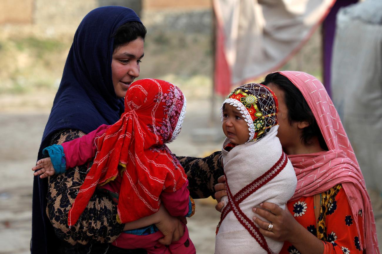 The photo shows two women talking and holding their babies up to also see face to face.