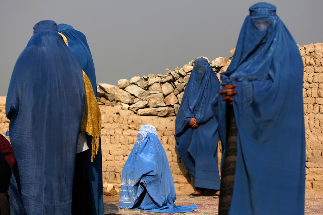 The photo shows several women in blue head coverings in front of a brown brick wall and a dark grey sky.