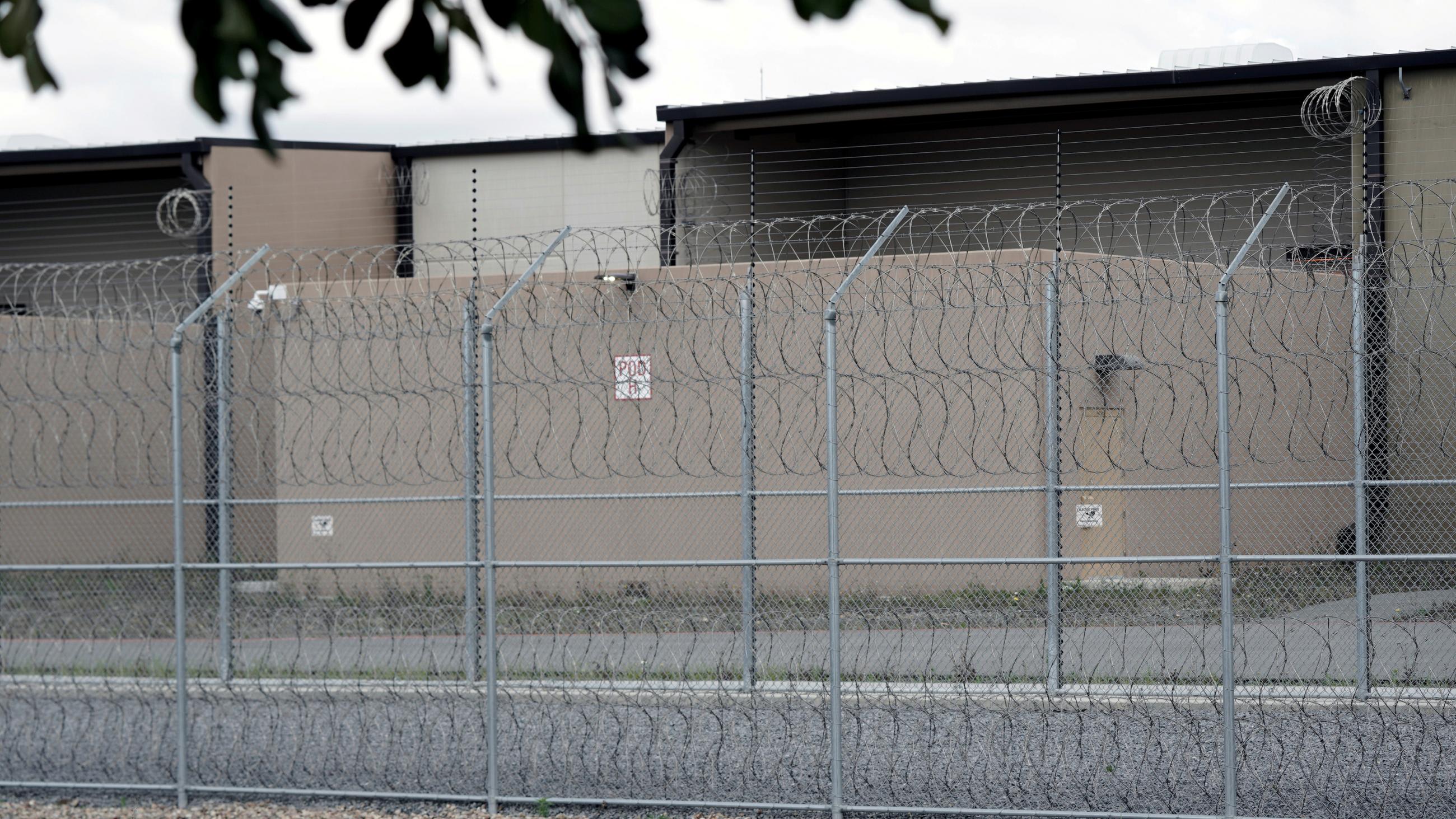 The photo shows a lockup from outside its perimeter barbed wire fence.