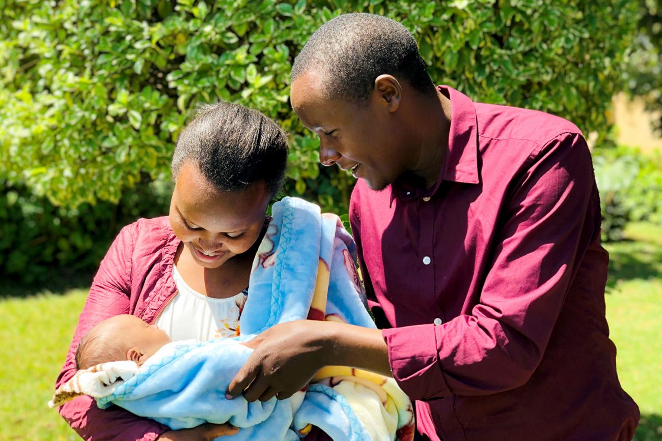 Picture shows a couple holding their newborn baby outside.
