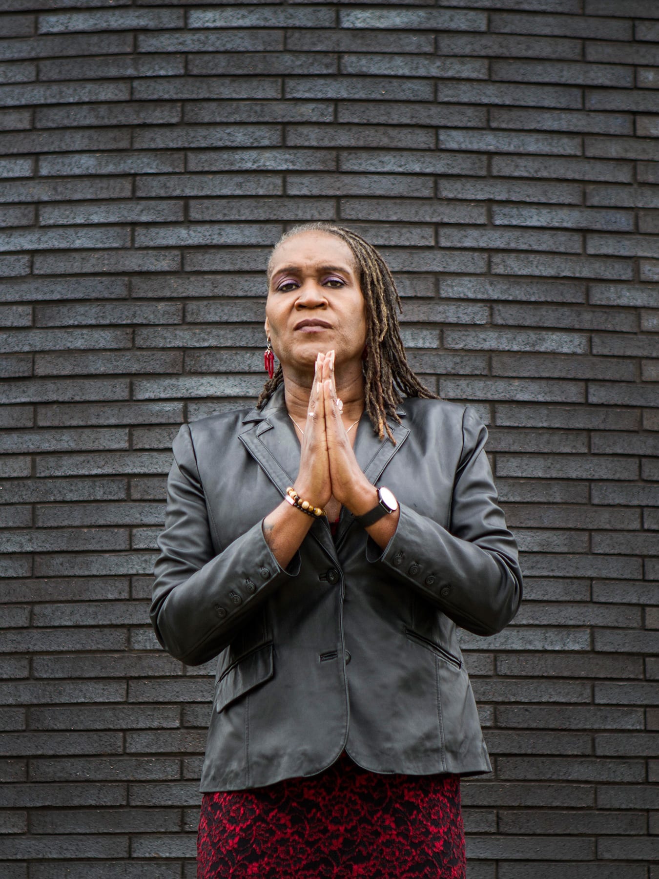 The photo shows the council vice president standing in front of a slate-colored brick wall with her hands together looking at the camera. 