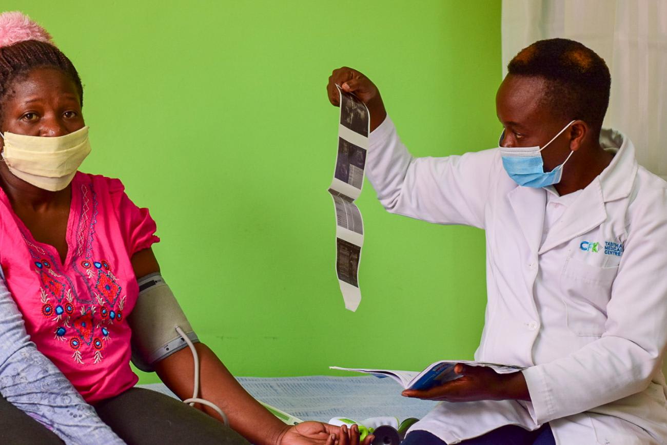 The photo shows the woman with a blood pressure cuff on her arm sitting on a hospital bed with b right green wall in the background. A doctor sits next to her holding what appears to be a series of ultrasound shots of a fetus. OPTIONS/Meshack Acholla