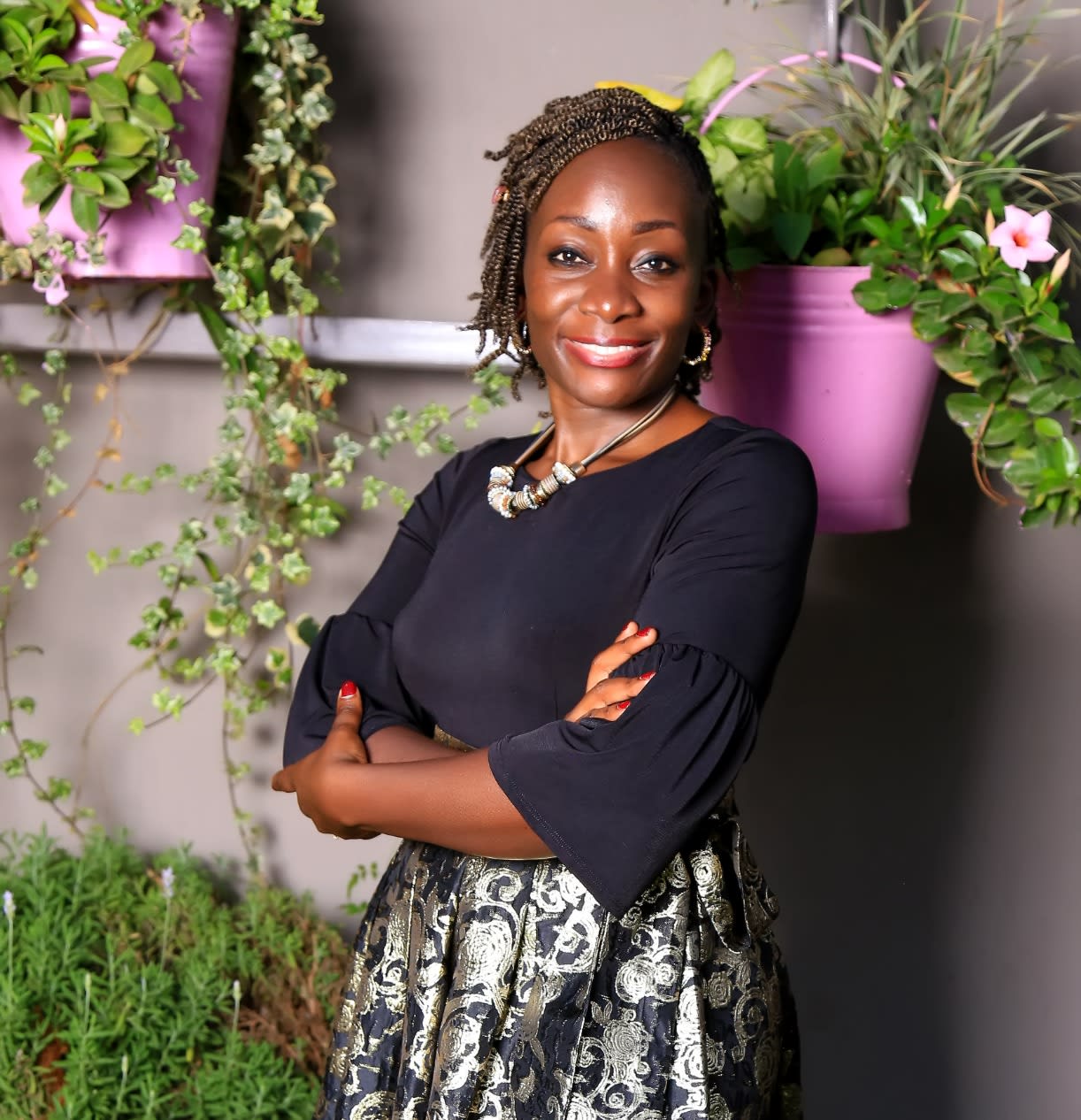 Dr. Liz Wangia poses against a wall with plants in lilac-colored pots. 