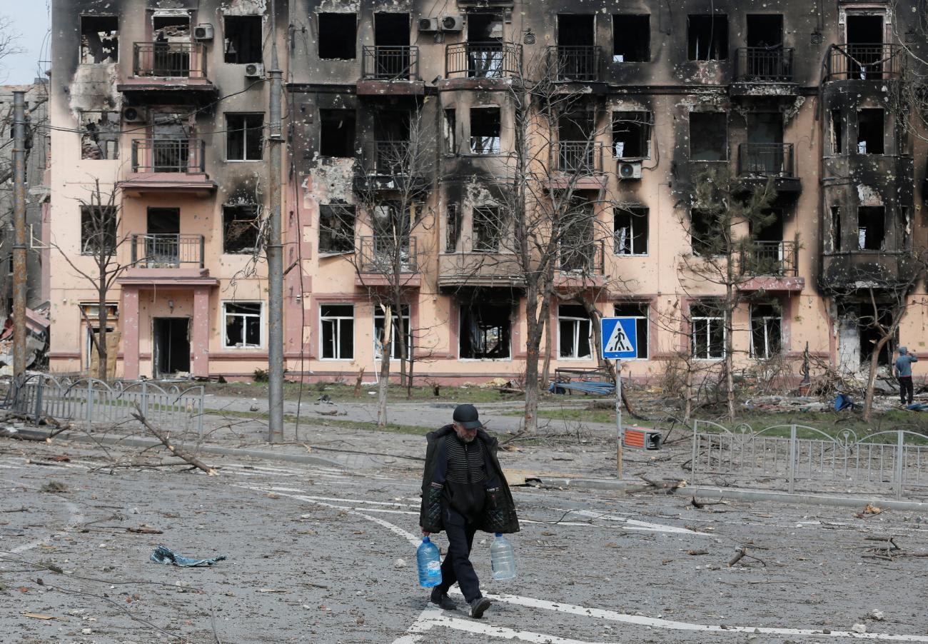 Cut off from water, a local resident carries bottles of water as he walks past a building charred and heavily damaged during Russia's attack on Ukraine's southern port city of Mariupol. Photo taken on April 3, 2022. 