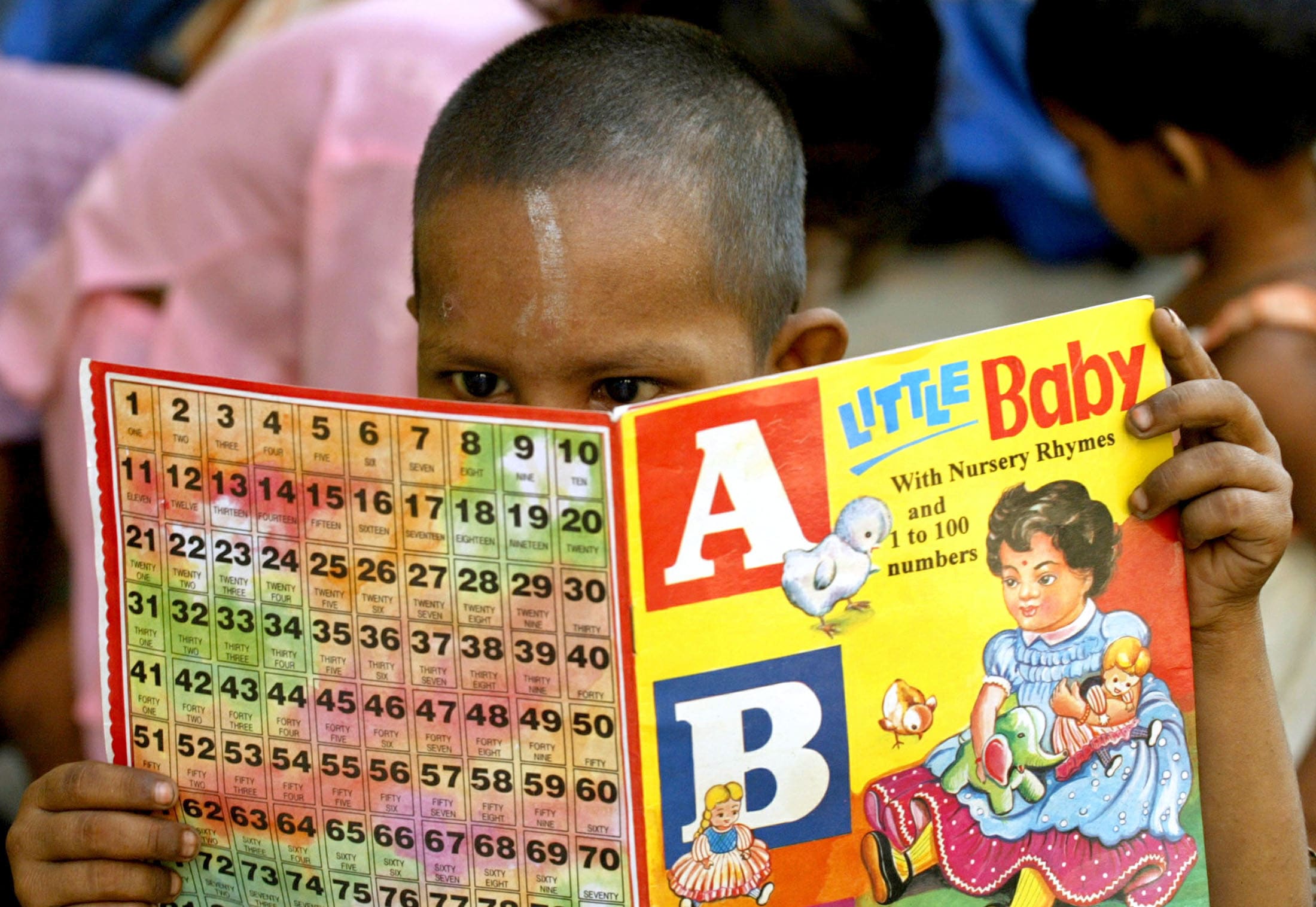 A boy with a shaved head reads an ABCs learning book with a yellow cover