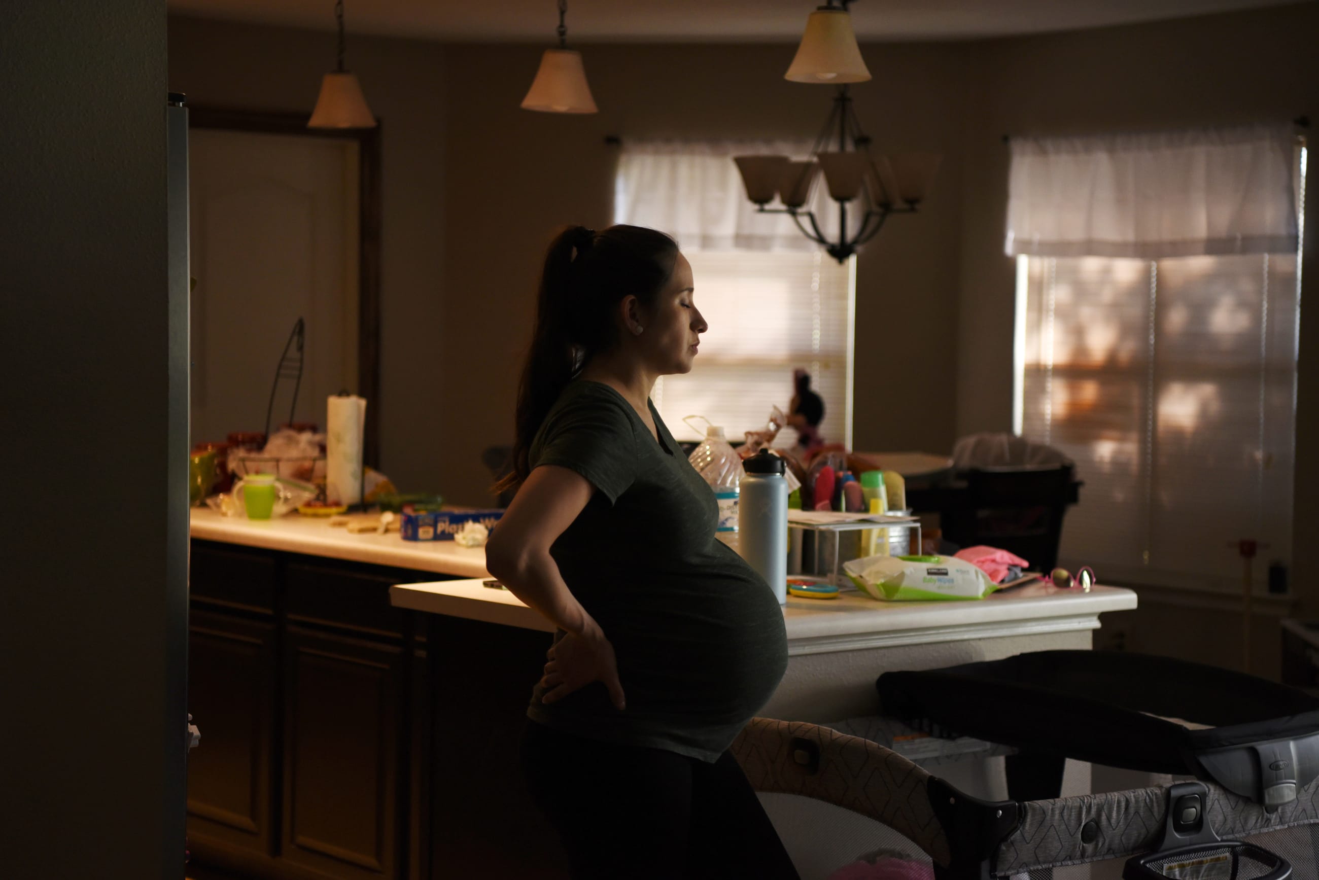 A pregnant woman stands in her kitchen.