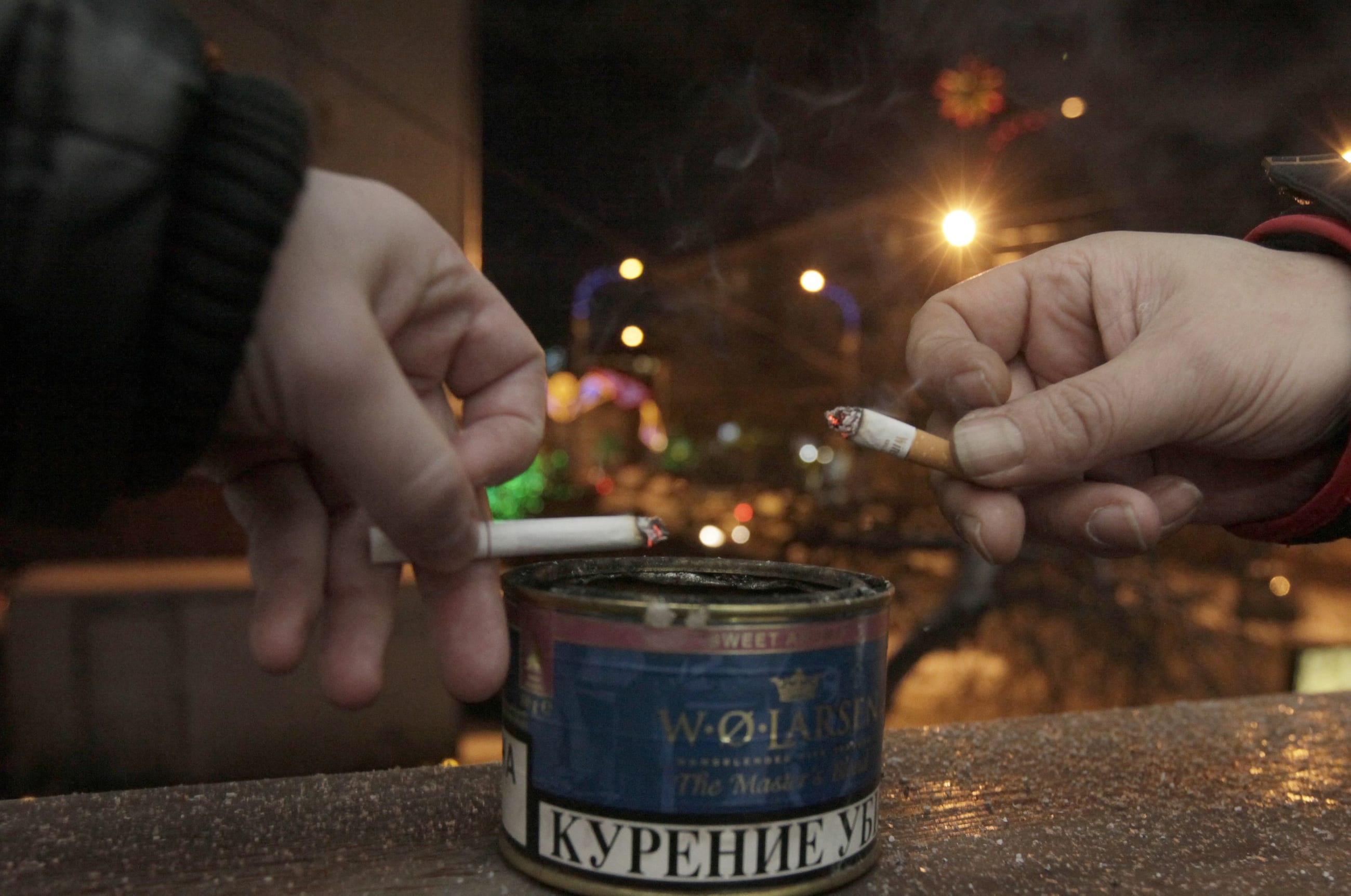 Men tap ash from their cigarettes while smoking on the balcony of an office building.