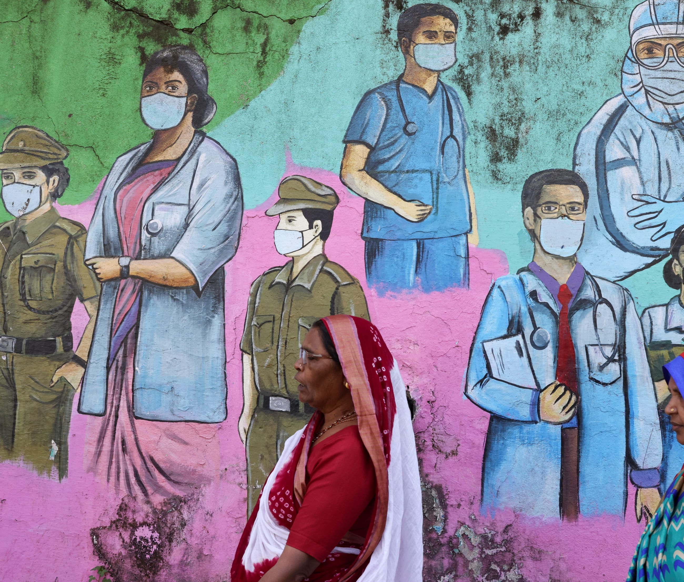 Women walk past a COVID-19 themed mural on the street.