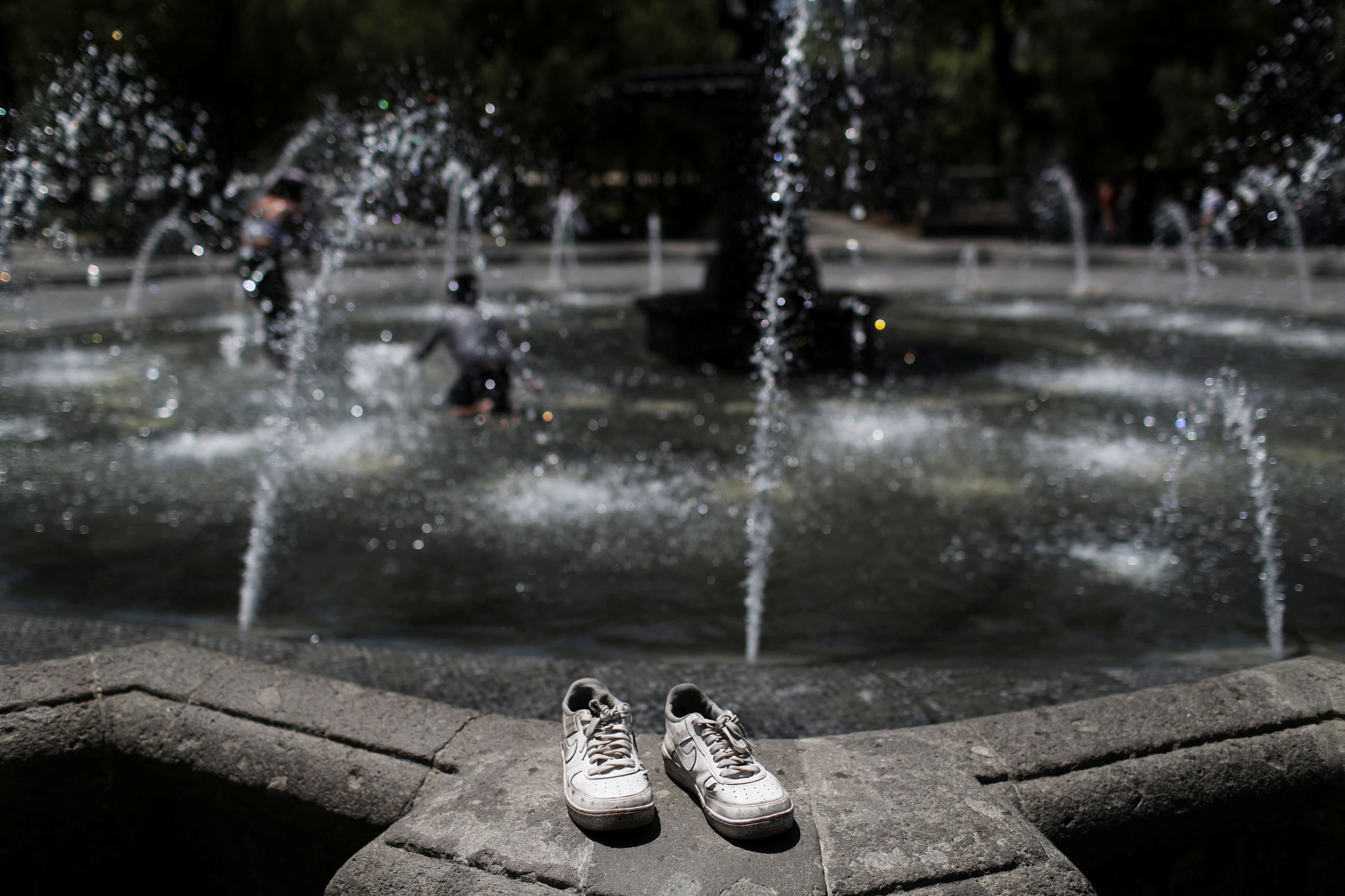 The tennis shoes rest on a fountain during a heat wave.
