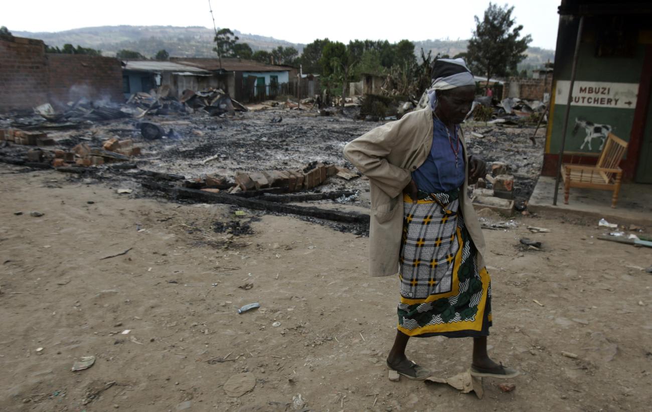 An elderly Kisii woman passes by the remains of a burned house.