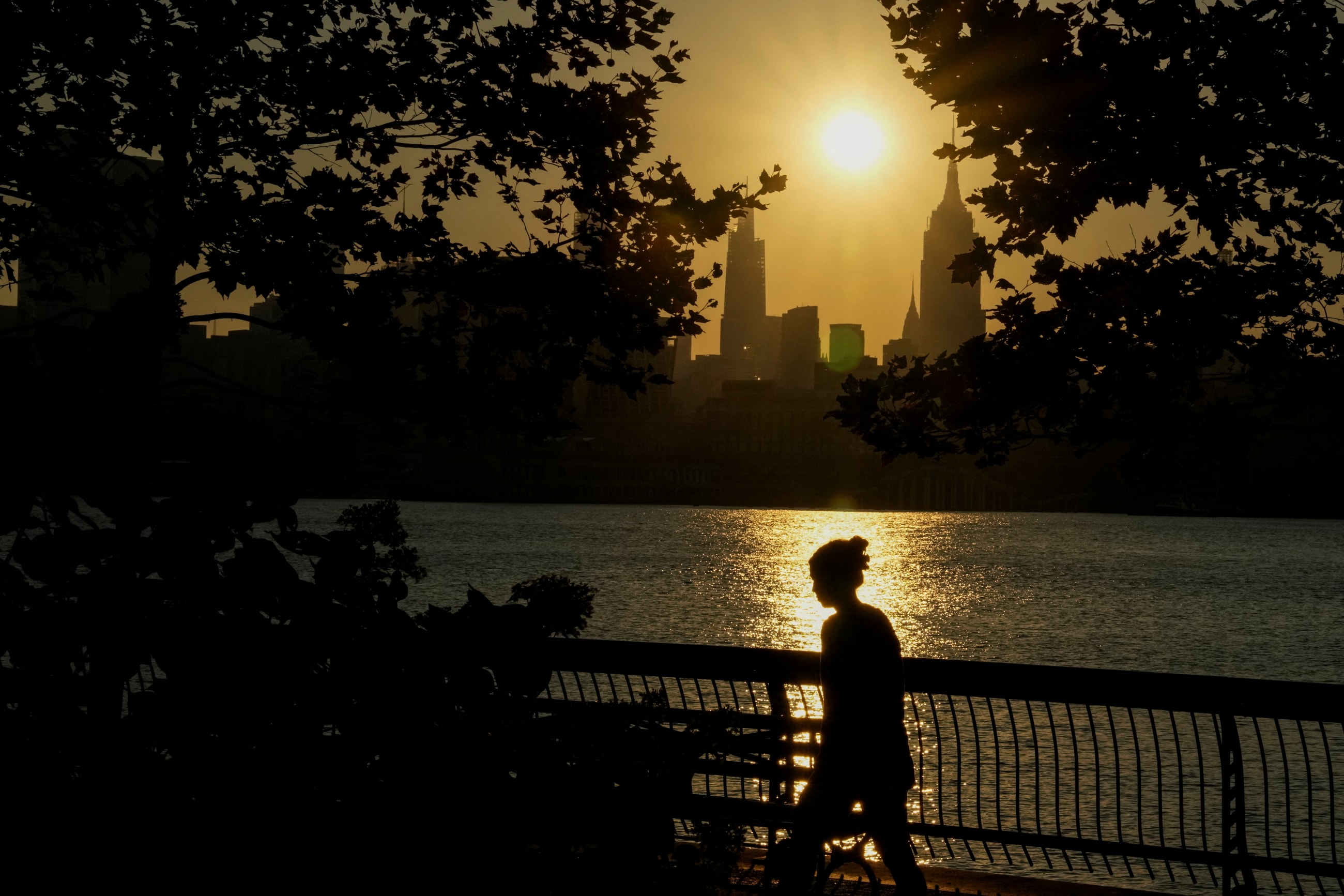 The sun rises over the New York City skyline as a person walks along the riverfront amid an extreme heat warning, in Hoboken, New Jersey, July 25, 2025