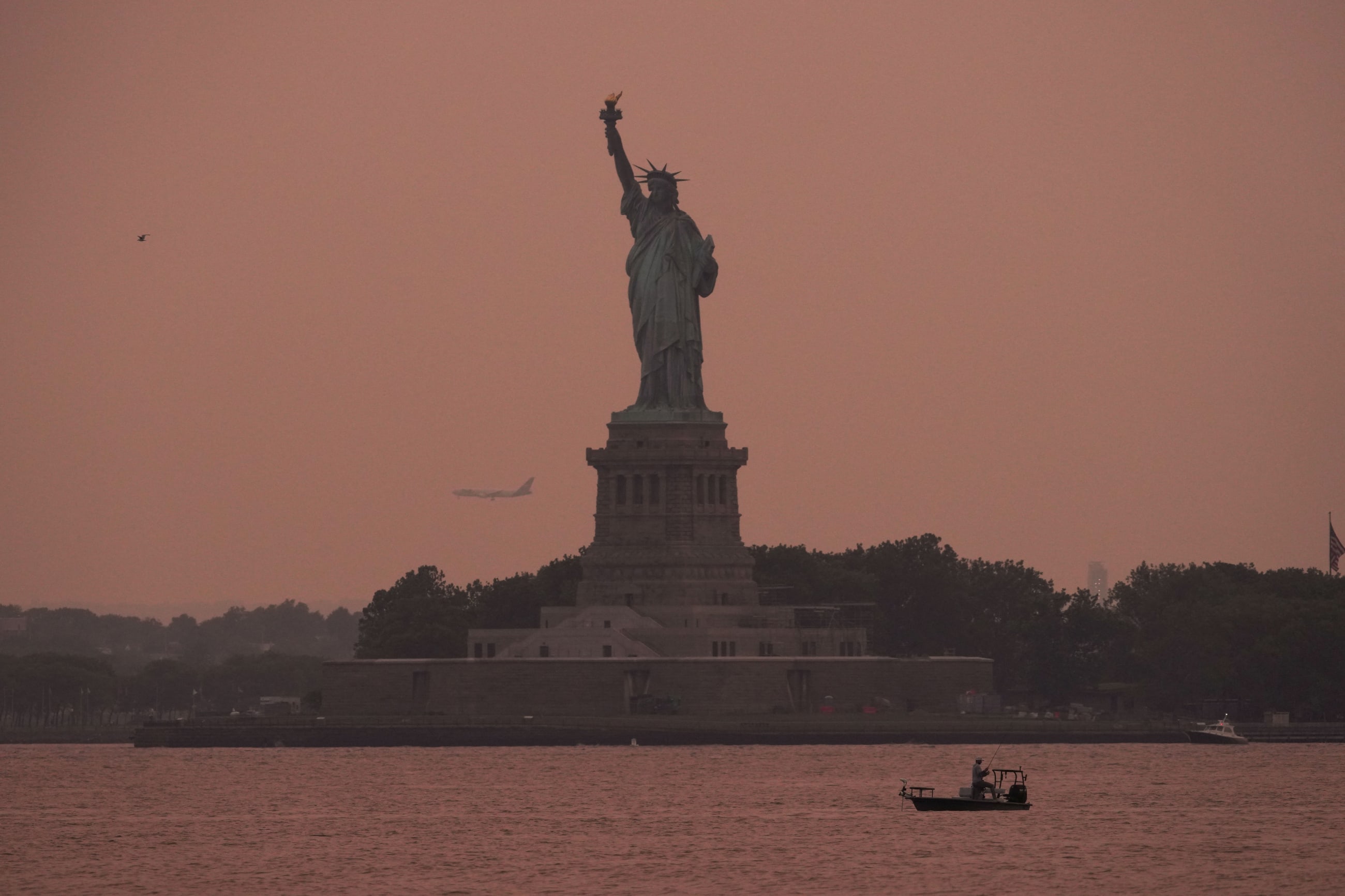 The Statue of Liberty is seen at sunset through haze caused by smoke from Canadian wildfires, as viewed from Brooklyn, New York, August 5, 2025.