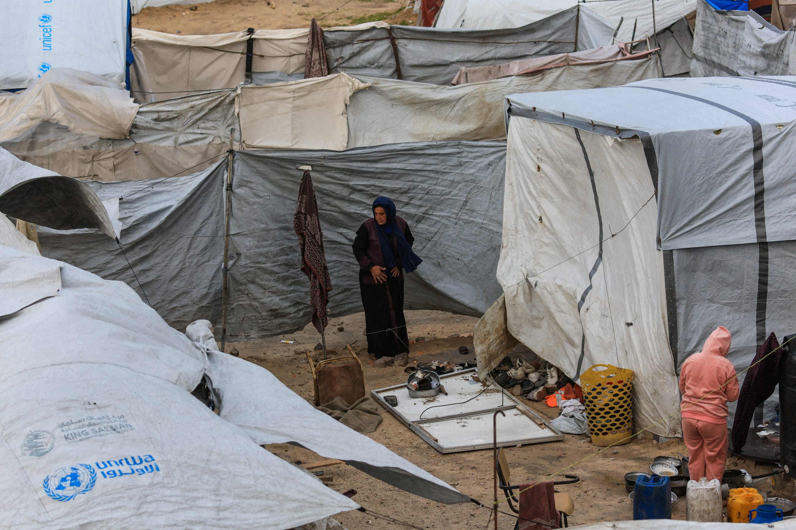A displaced Palestinian woman stands among tents, during a windy winter day, in Gaza City, on January 13, 2026.