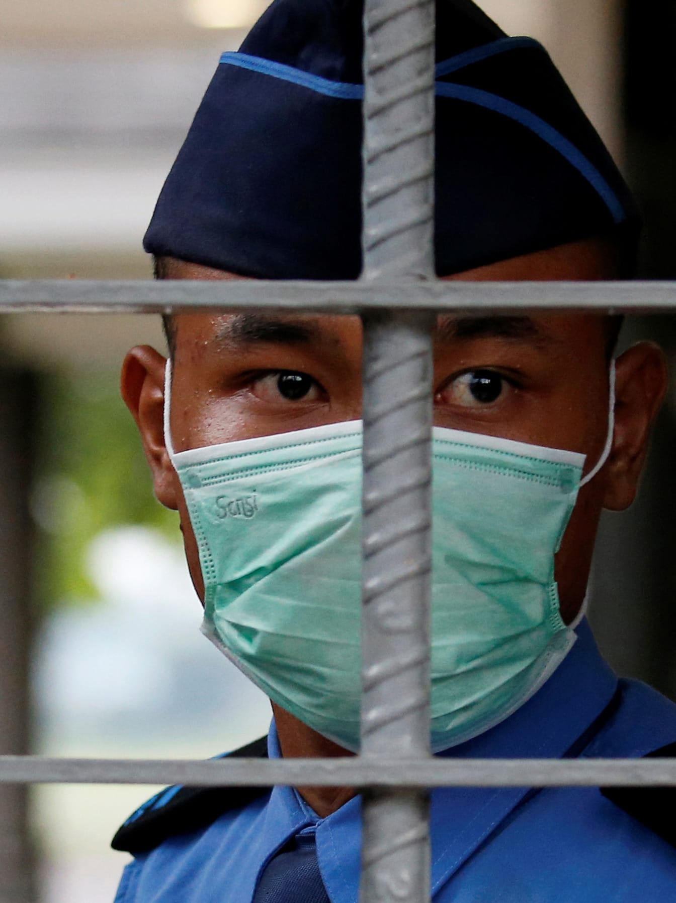An aviation security officer wearing a protective mask stands guard at Halim Perdanakusuma airport, following the outbreak of the coronavirus in China, in Jakarta, Indonesia on February 15, 2020. Photo shows a uniformed officer behind some bars wearing a mask.