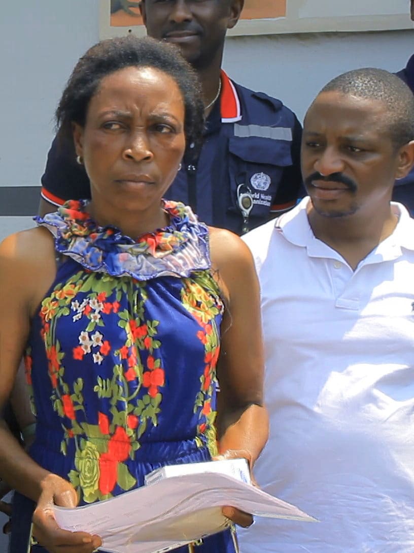 The photo shows the former patient looking to the side of the frame with a serious look on her face as she is surrounded by people who are looking at her.