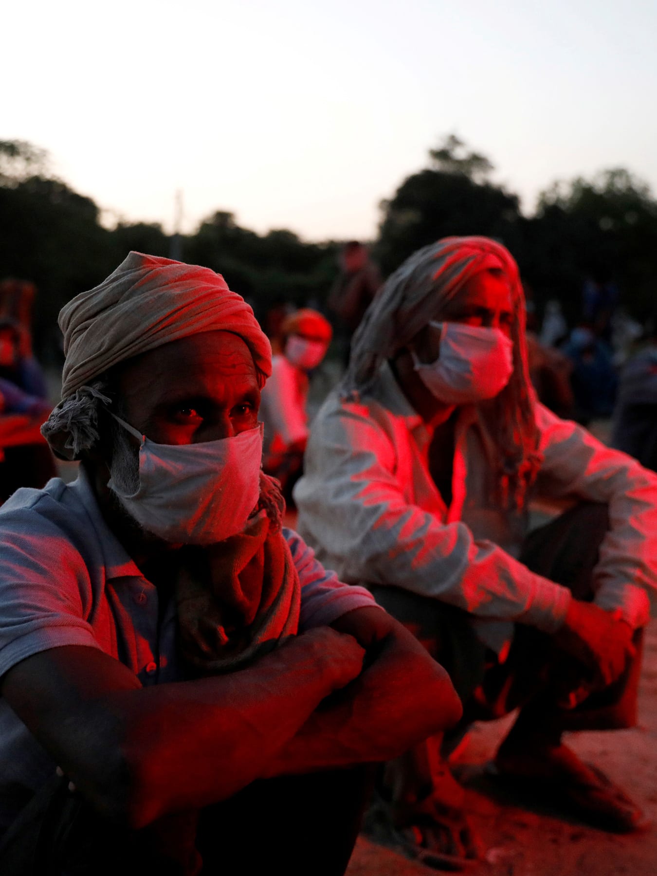 This is an eerie and haunting photo with several people sitting on the ground in an outdoor location in low lighting. They are bathed in a dark red light.