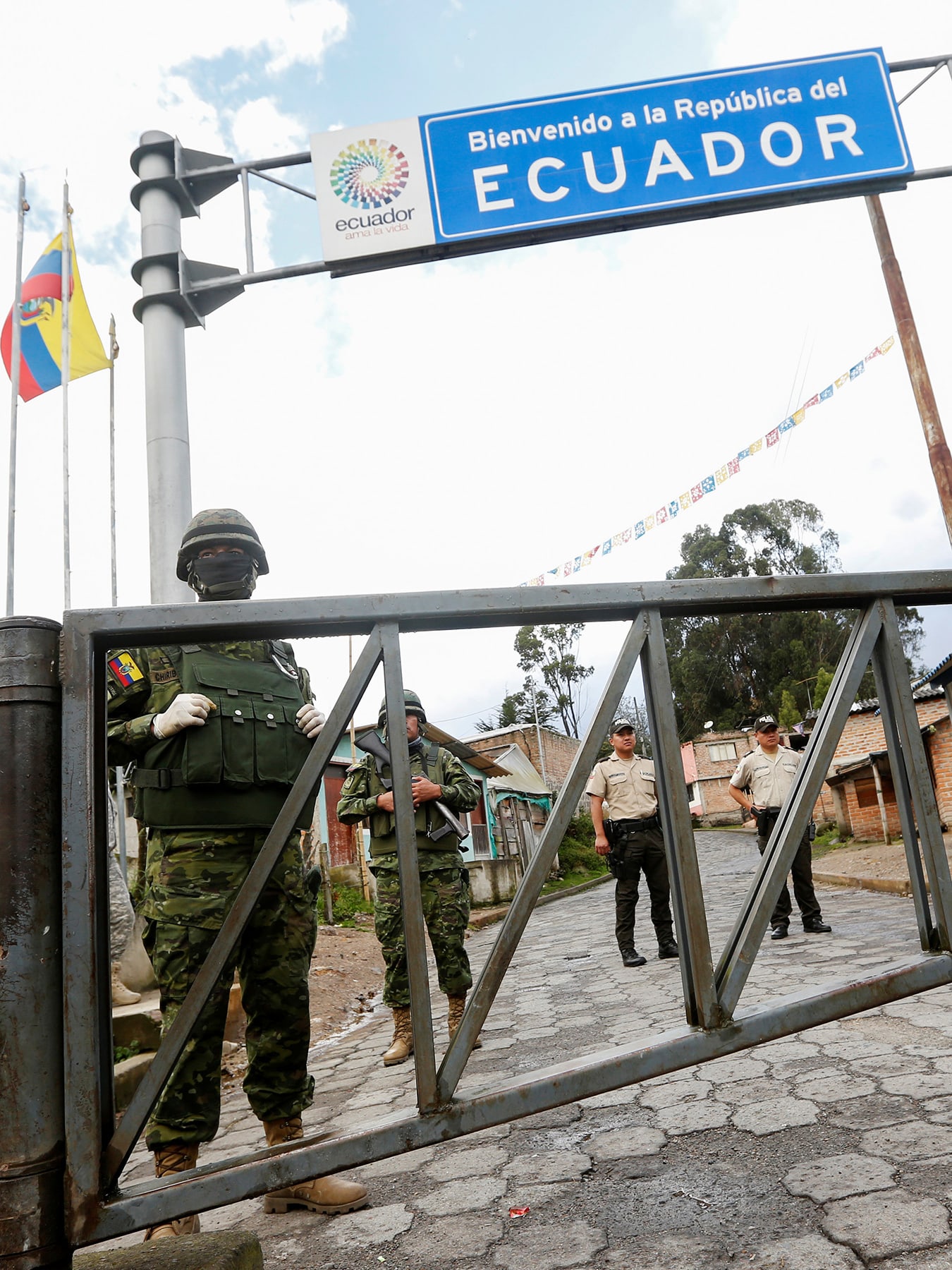 The photo shows a border crossing with a large sign reading, Ecuador, and several soldiers in the frame.