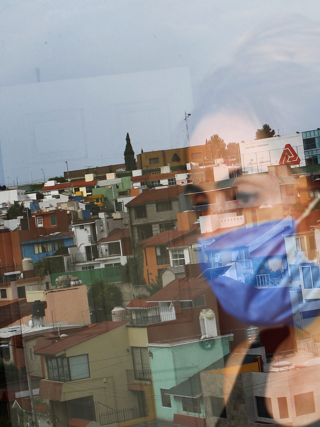 Picture shows the woman looking out her window and partially reflected in the glass.