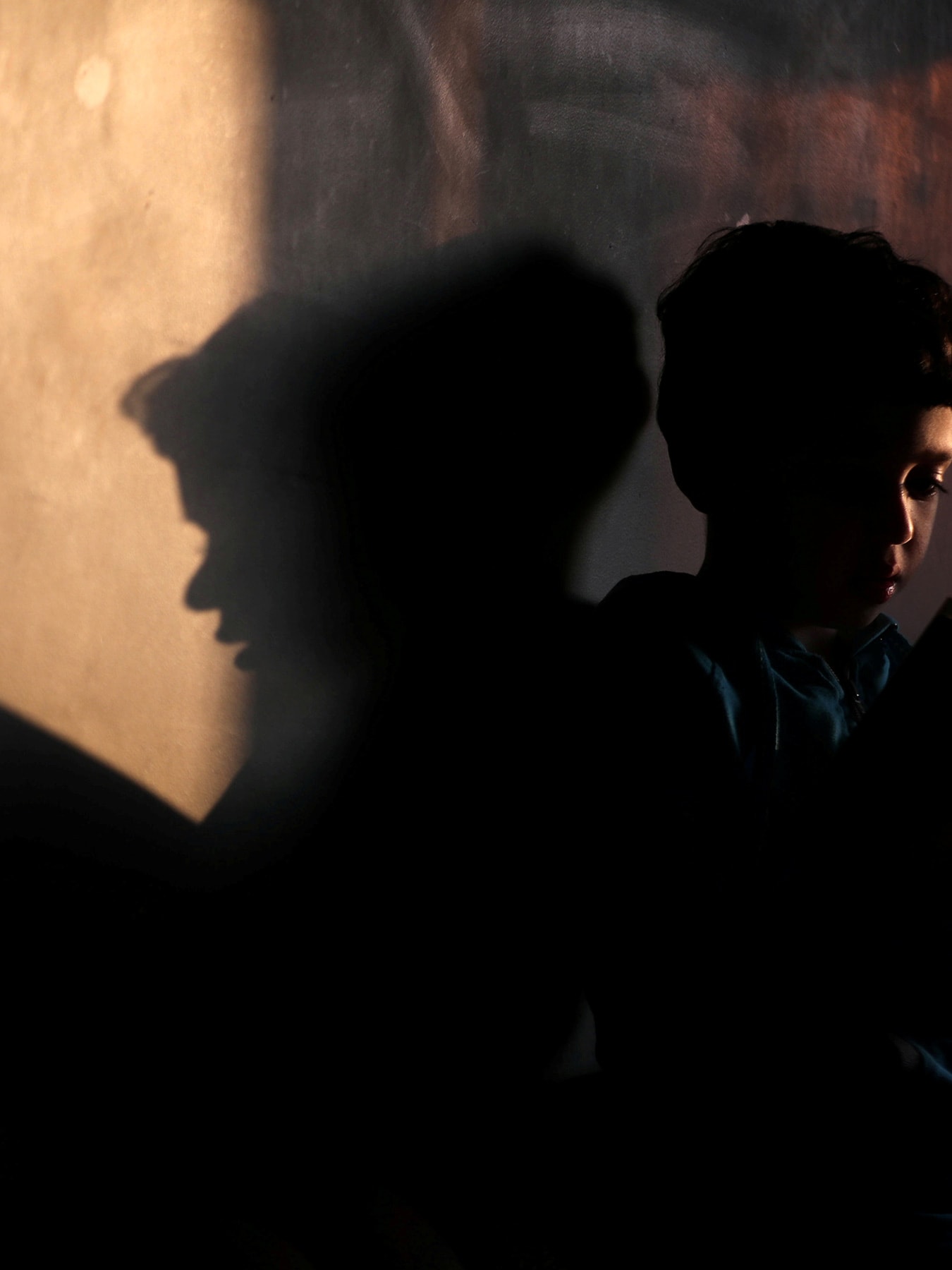 Picture shows the boy reading with his shadow cast on the wall behind him.