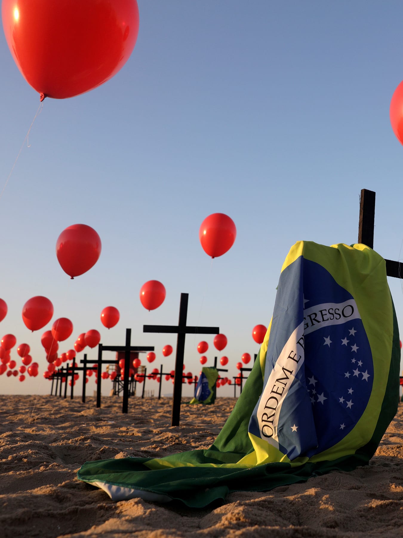 The photo shows an art installation of crosses, balloons and flag on the beach.