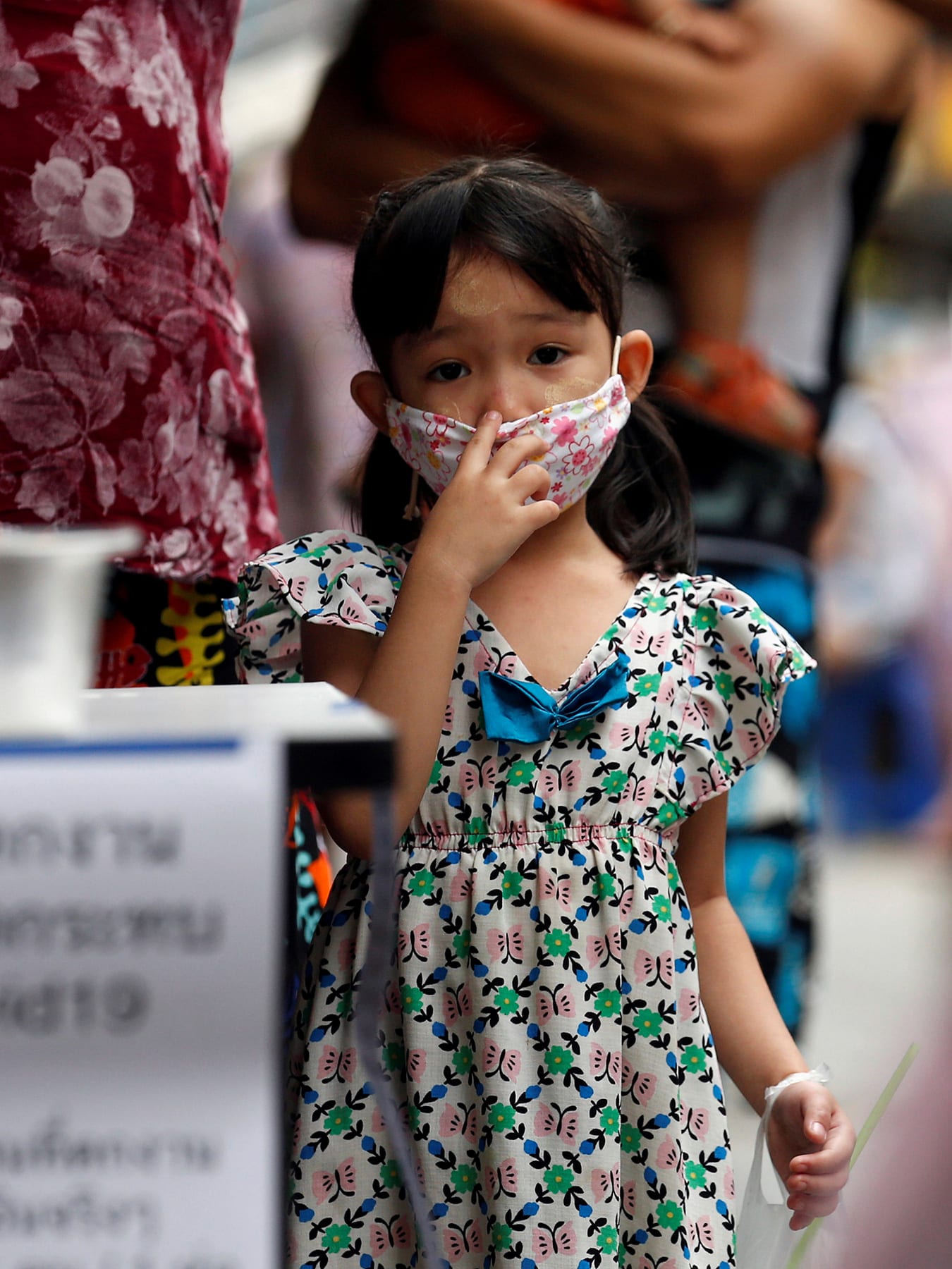 The photo shows a small girl wearing a facemask looking at the camera.