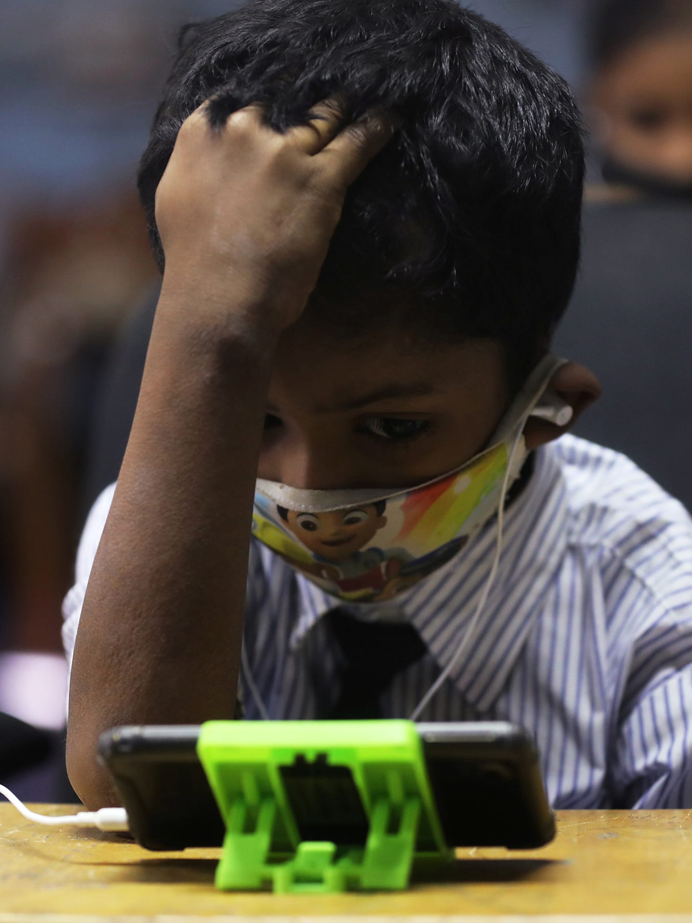 The photo shows a small child at a school desk with a mobile phone on the table in front of them.
