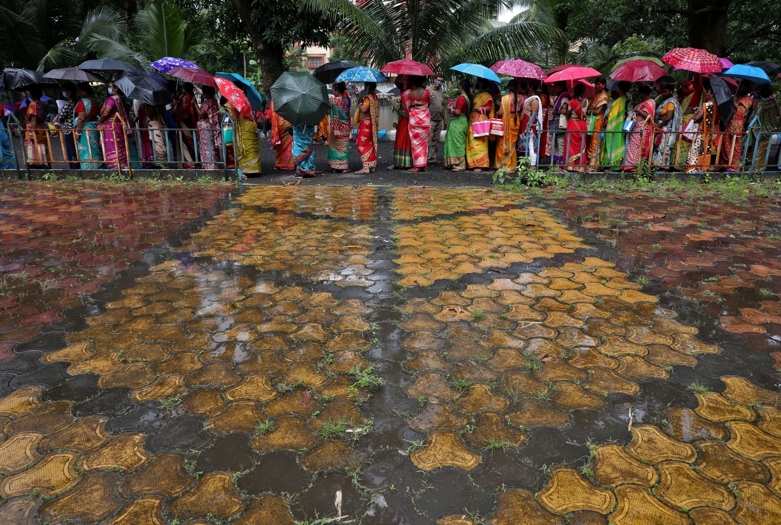 Women hold umbrellas to cover from rain as they wait to receive a dose of COVISHIELD vaccine, a COVID-19 vaccine made by Serum Institute of India, at a vaccination centre in Kolkata, India, August 31, 2021.