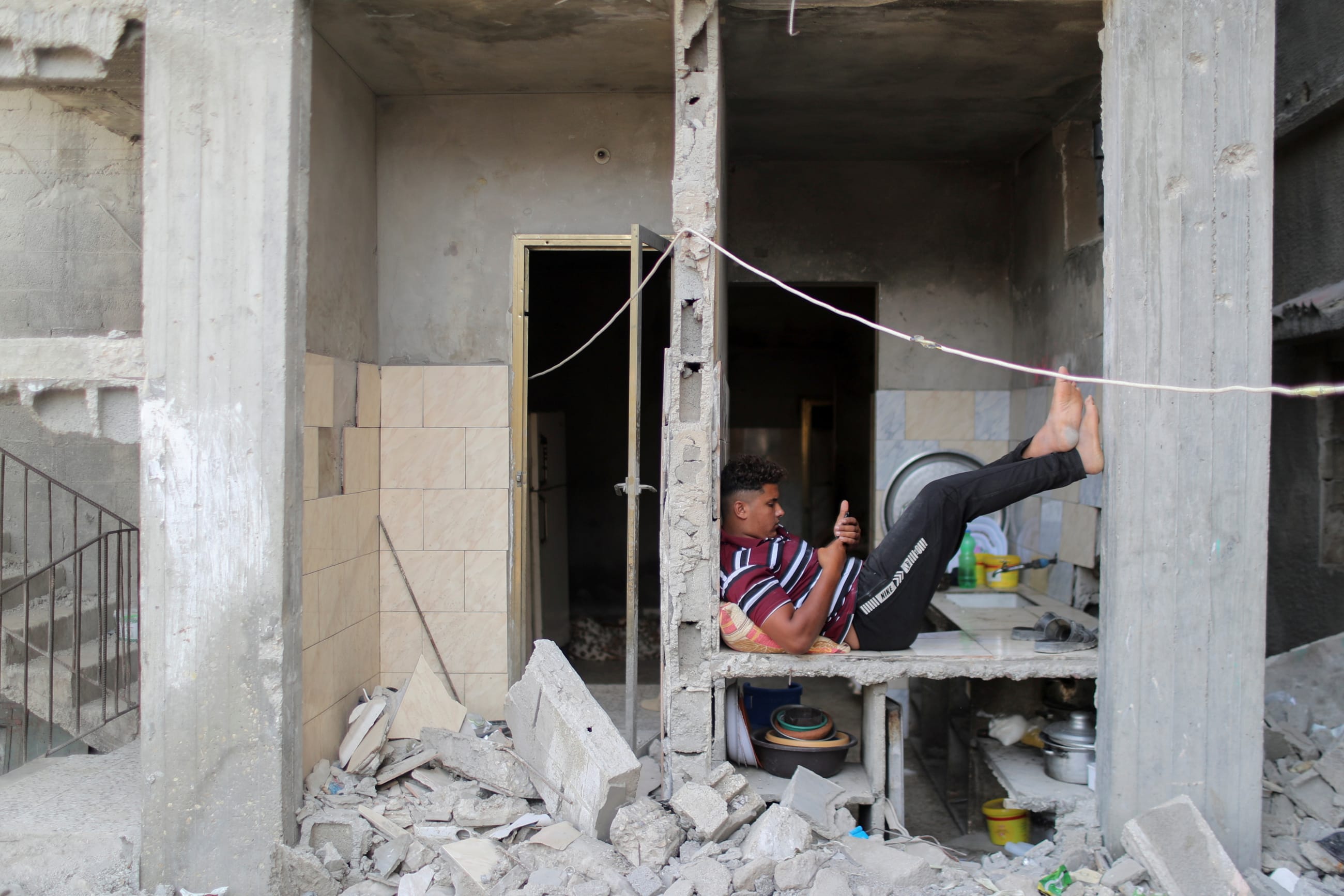 A Palestinian uses his phone as he sits amid the rubble of a house that was destroyed in Israeli air strikes during Israeli-Palestinian fighting, in Gaza June 9, 2021.