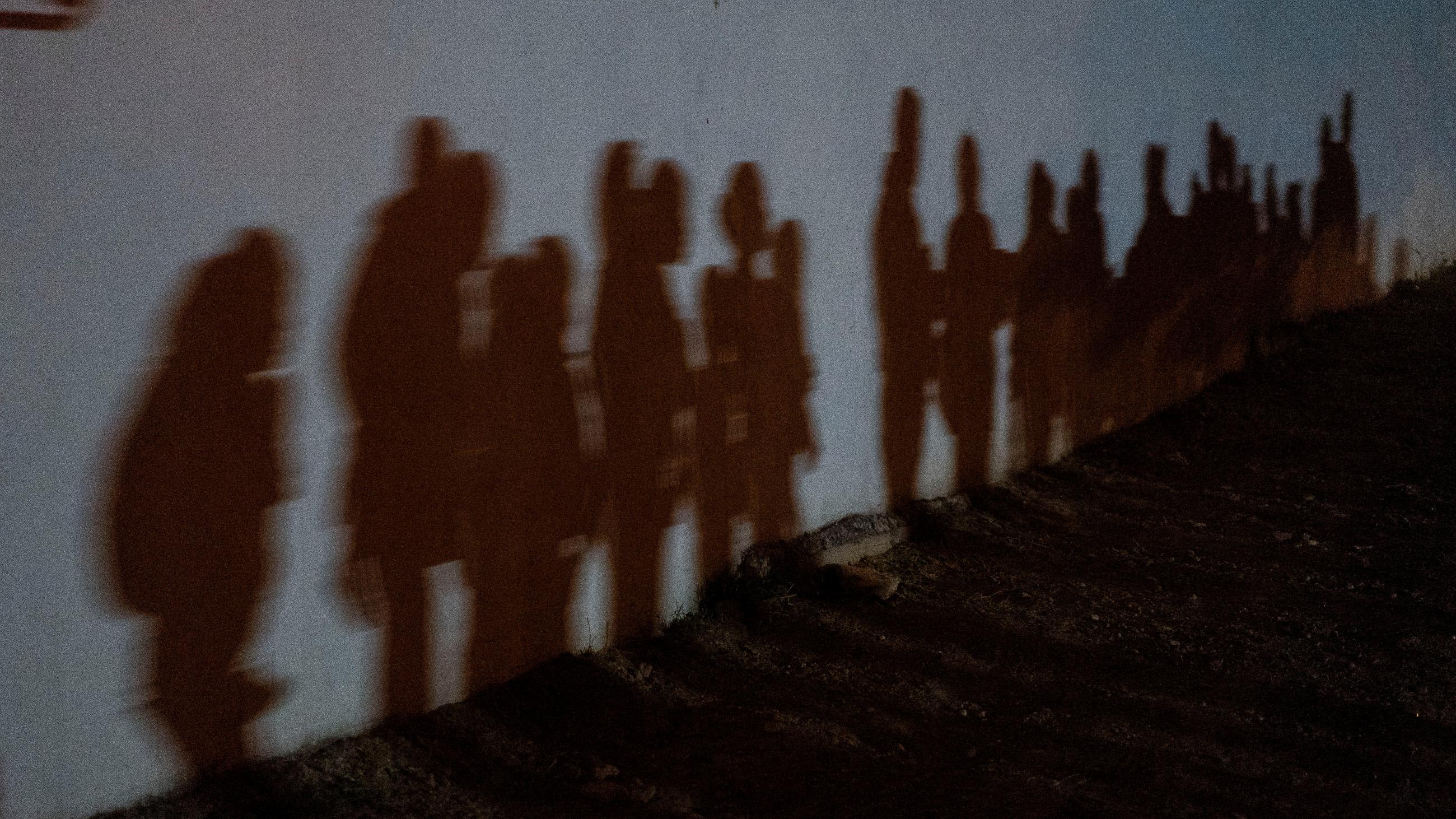 Shadows on a wall show asylum-seeking families as they queue up to be processed by the U.S. Border Patrol after crossing the Rio Grande River from Mexico, in Roma, Texas on August 12, 2021.