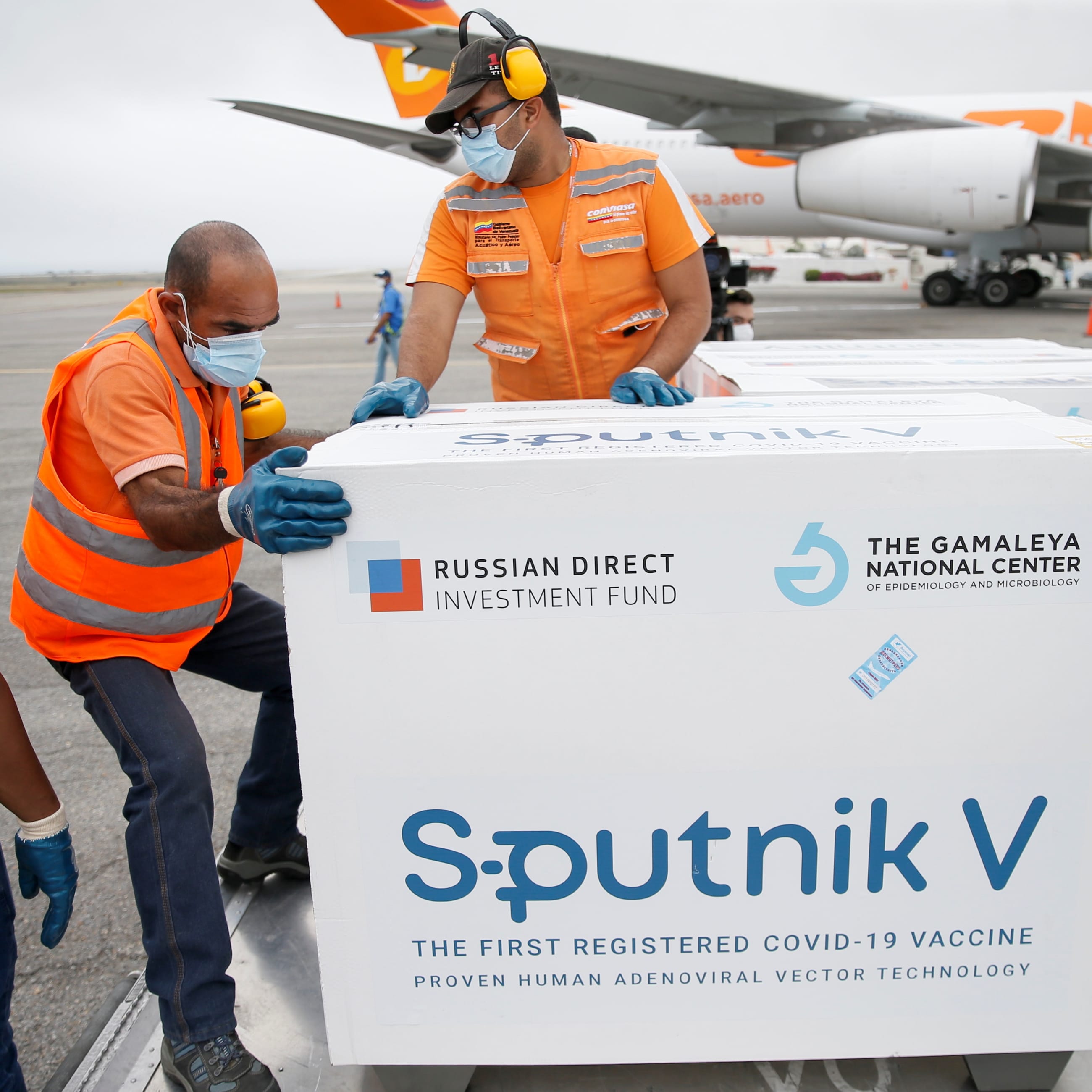 Airport workers in orange vests unload crates of the Sputnik V vaccine at an airport in Caracas, Venezuela