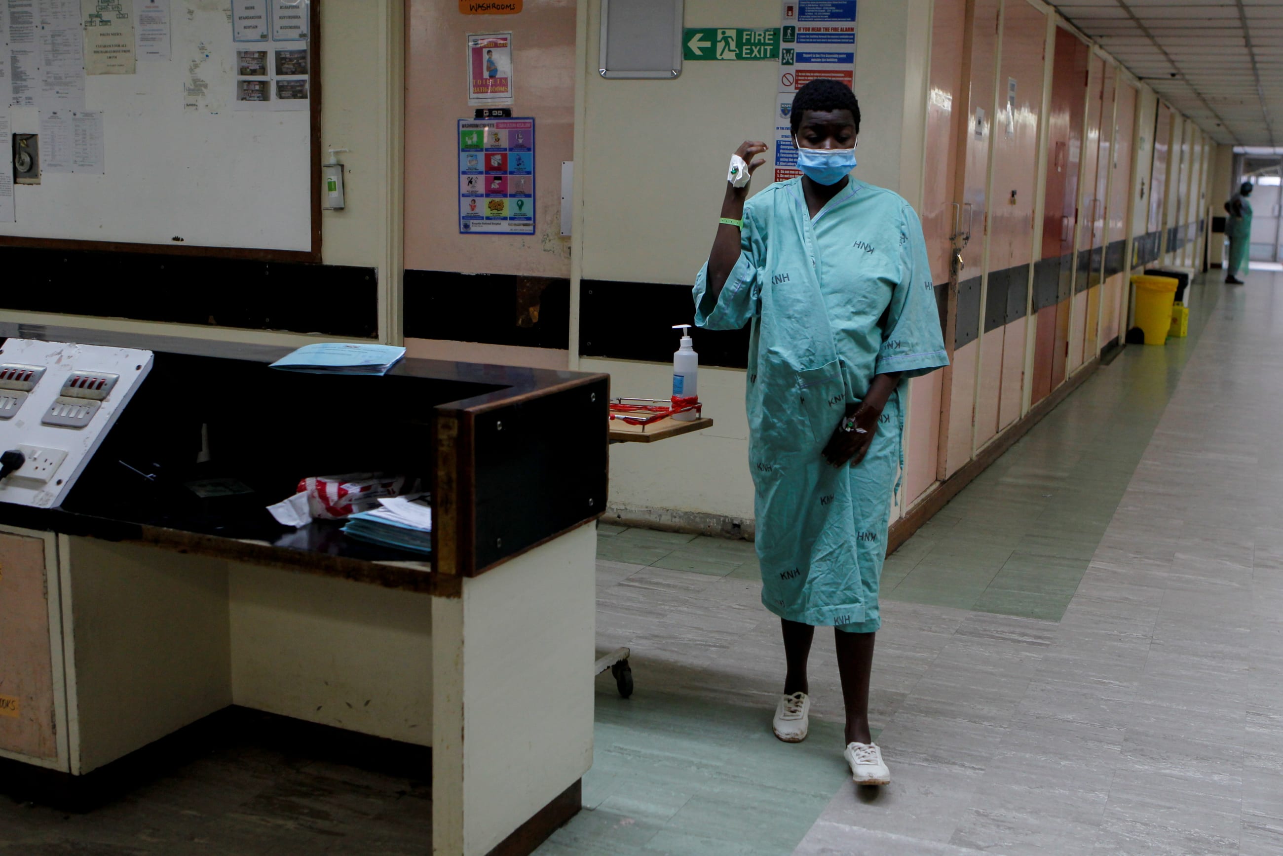 A young woman wearing a blue hospital gown and white surgical face mask walks through the halls of Kenyatta National Hospital after giving birth in Nairobi, Kenya