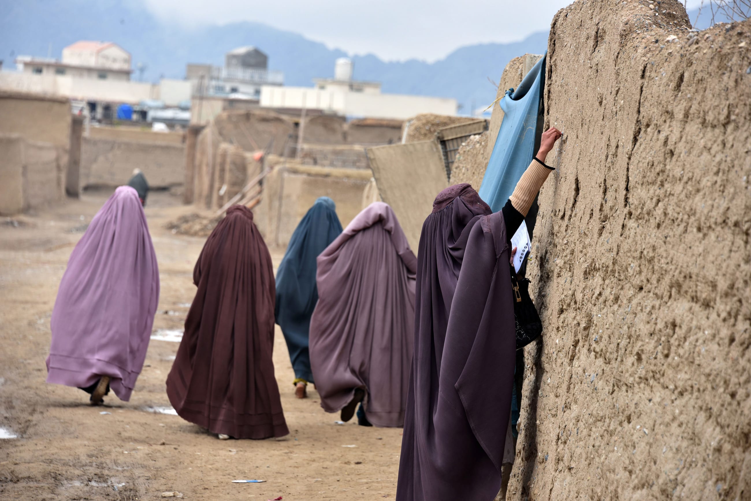 Women in lavender, blue, and burgundy burqas who are part of an immunization team write a message on the wall of a stone house during a vaccination campaign in Kandahar, Afghanistan, on January 28, 2020.