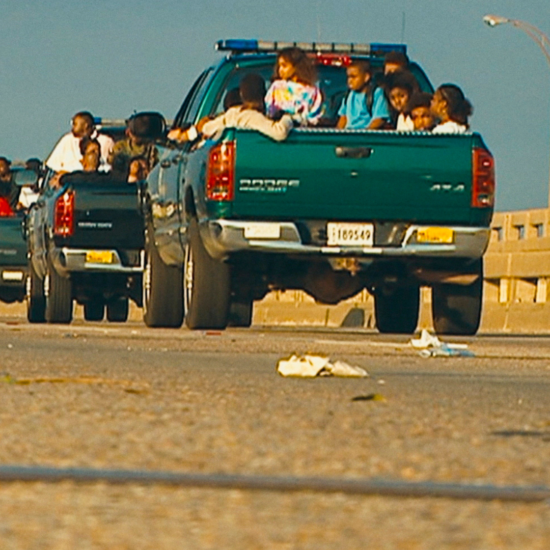 A caravan of green trucks carry child evacuees displaced during Hurricane Katrina, New Orleans, Louisiana, August 2005. Photo courtesy of HBO/Katrina Babiess