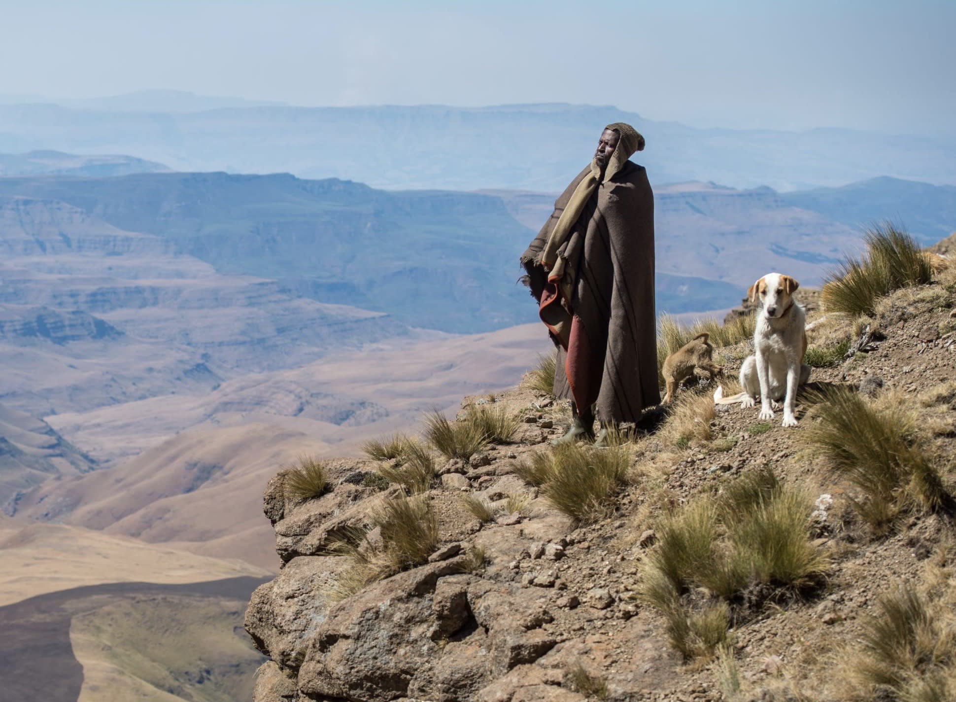 Basotho shepherd and dog looking out from a mountain ledge, in Thaba Tseka, Lesotho.