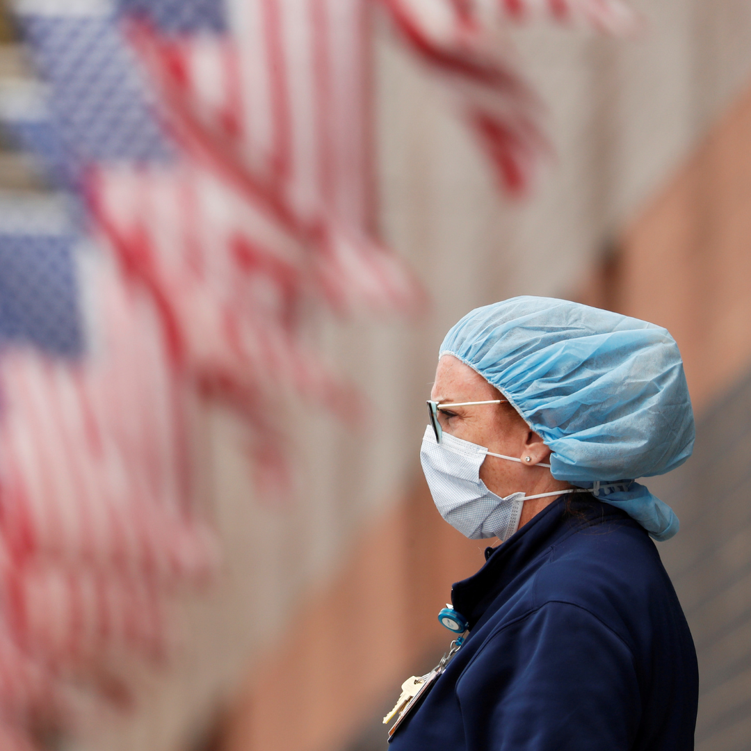 A nurse, seen in profile with a long row of American flags behind her, watches an ambulance driving away outside of Elmhurst Hospital during the COVID-19 pandemic, in Queens, New York, on April 20, 2020.