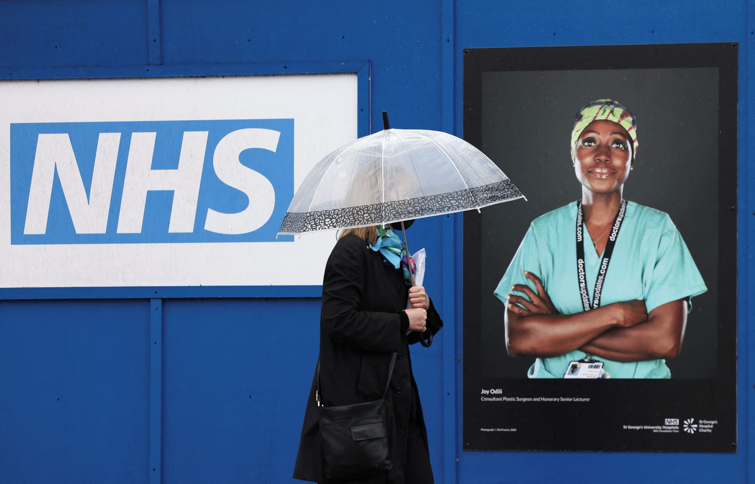 A woman walks past a poster of a NHS worker displayed on hoardings outside a temporary field hospital at St. George's Hospital, in London, Britain, on January 8, 2022.