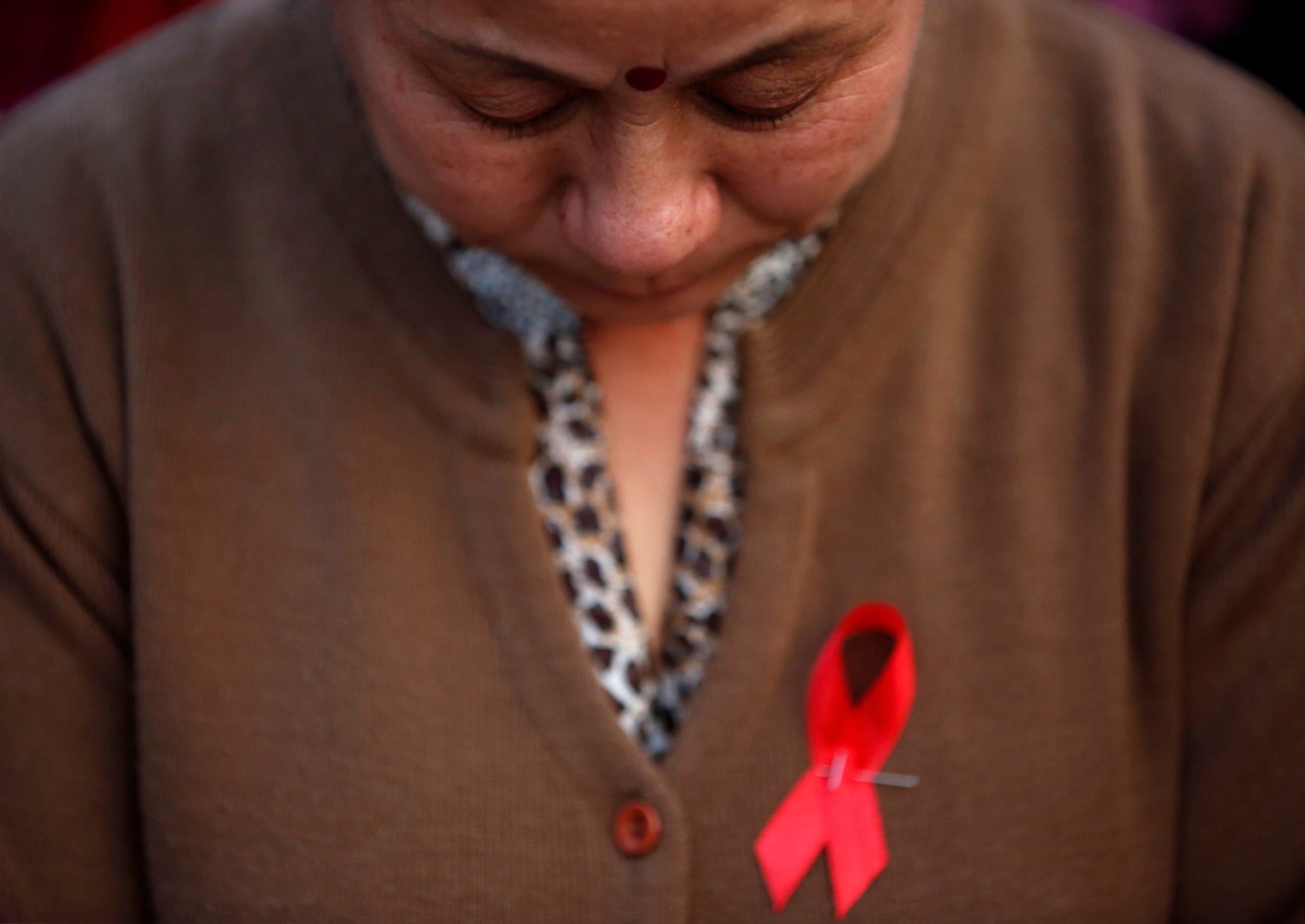 A participant with a red ribbon pin observes a minute of silence during a HIV/AIDS awareness campaign.