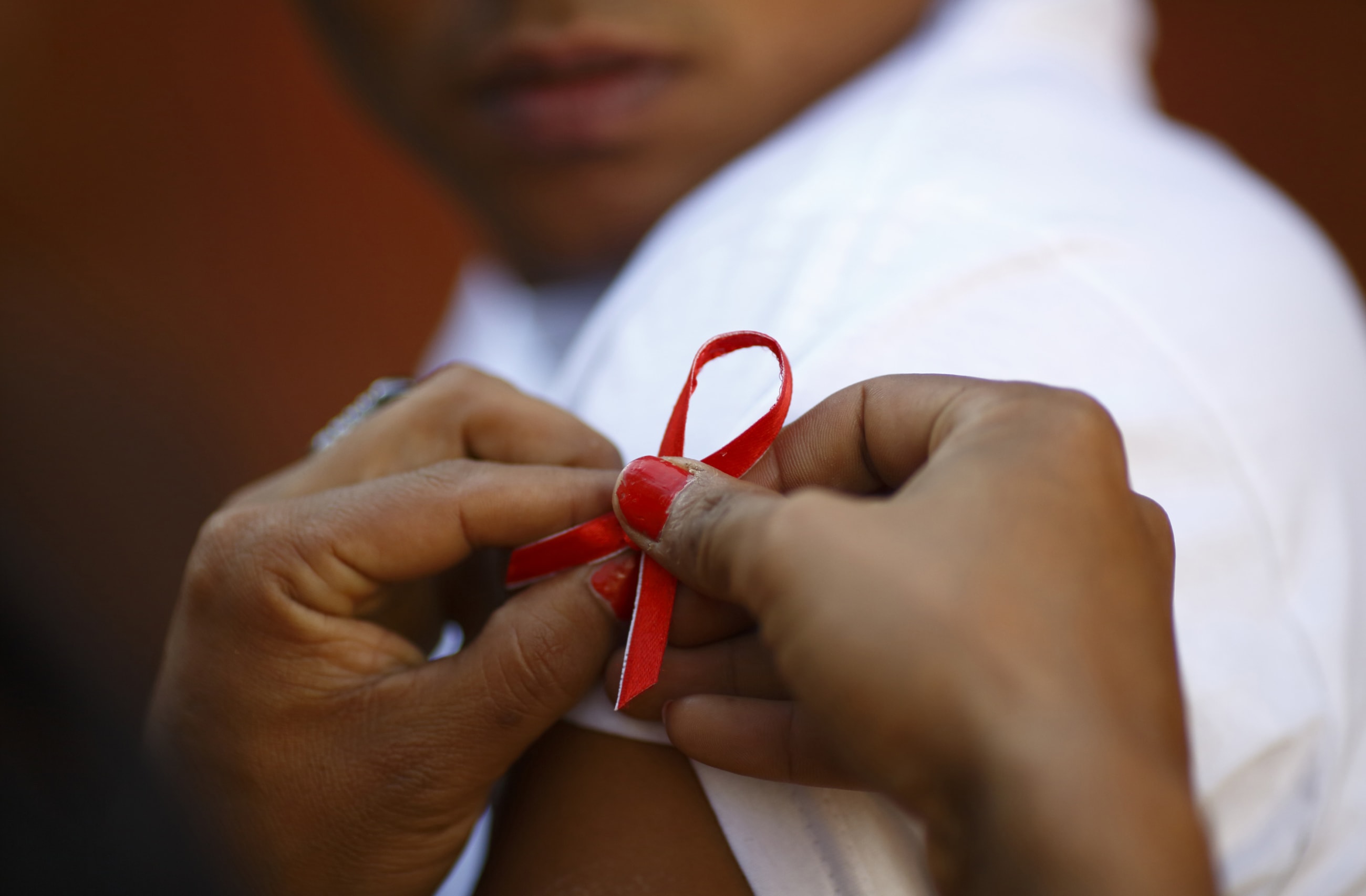 A red ribbon is put on the sleeves of a man by his friend to show support for people living with HIV, in Kathmandu, Nepal, on December 1, 2013.