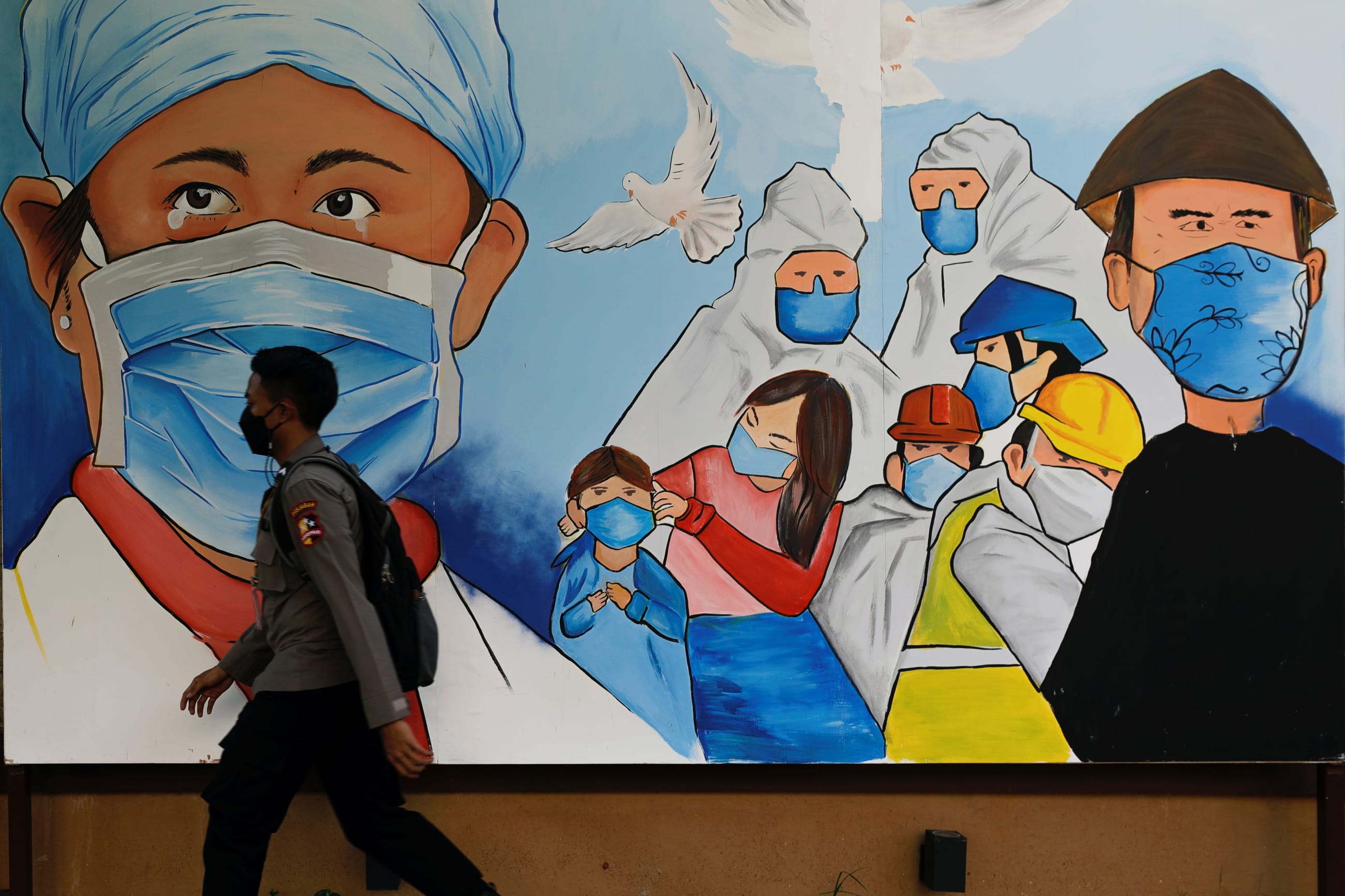A police officer walks past a mural promoting the use of protective face masks, in Jakarta, Indonesia, on December 2, 2021.
