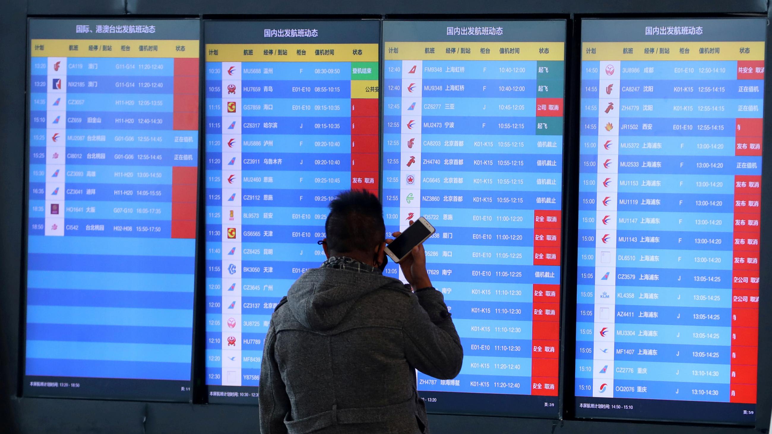 A man stands in front of an airport screen showing multiple flight departure cancellations after the city was locked down following the outbreak of a new coronavirus in Wuhan, China on Jan 23, 2020.